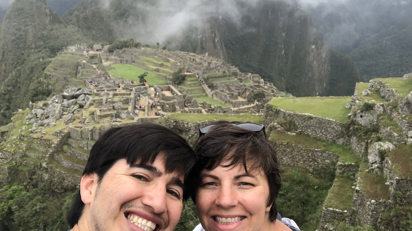 A man and a woman pose for the camera with the Inca ruins of Machu Picchu in the background.