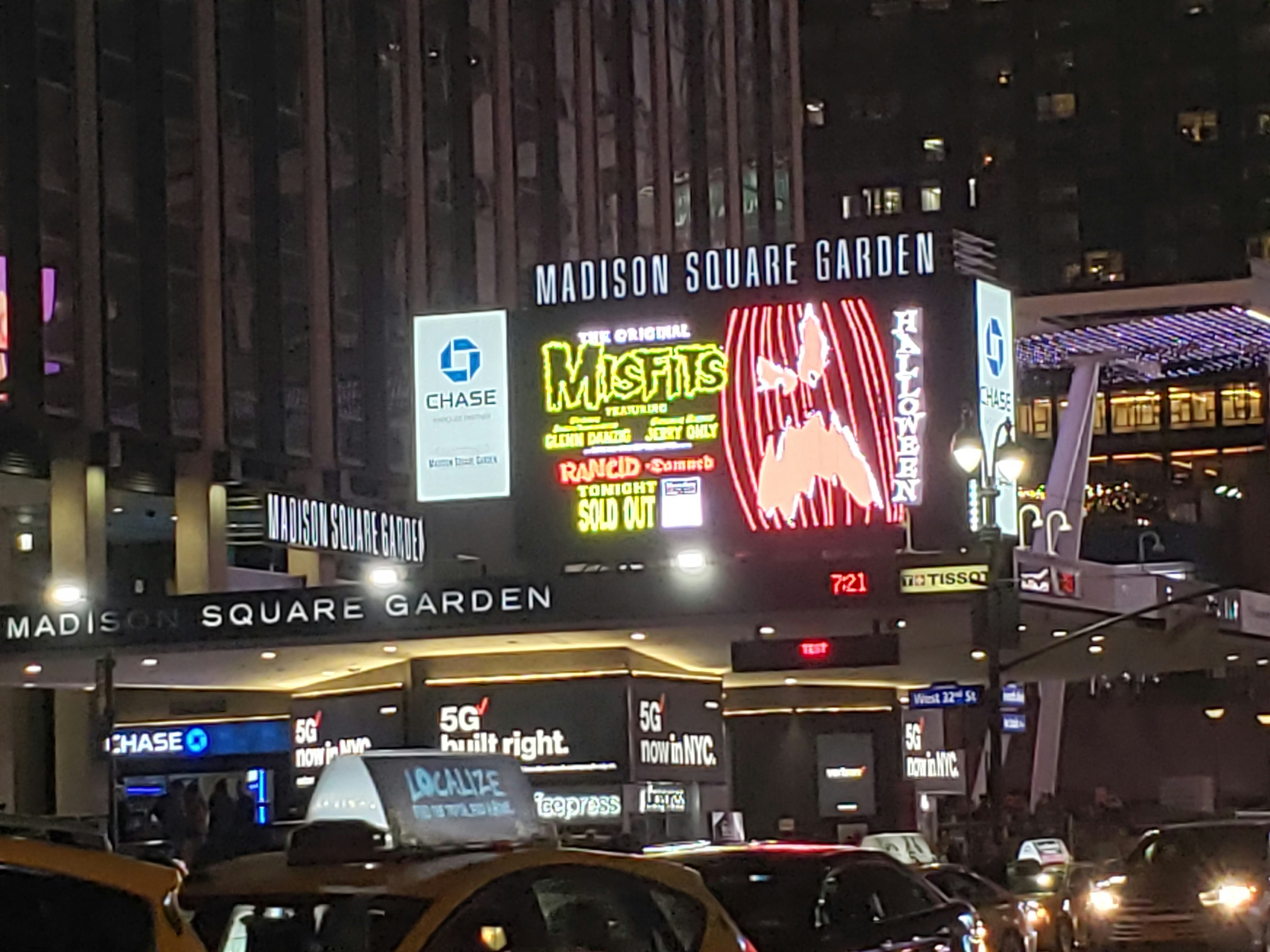 The bright lights of Madison Square Garden advertise a Misfits concert with Rancid over a line of taxi cabs in the street.