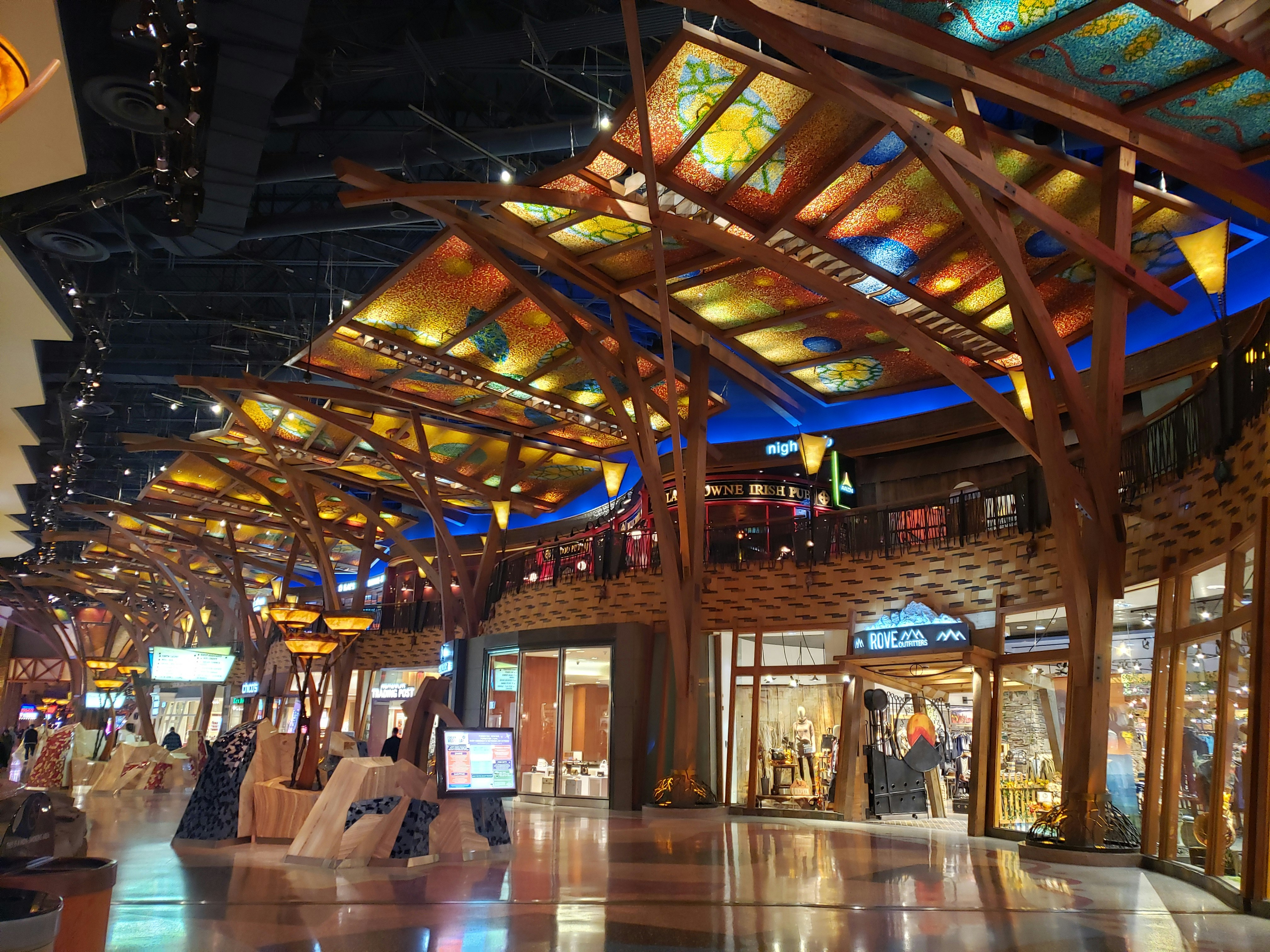 The mall in Mohegan Sun Casino is made up of rows of storefronts, over which is a wrought-iron railing marking the second floor, where signs from more shops and an Irish pub gleam. Over the first-floor walkway are large stained glass awnings in colors of red, yellow, and blue in a blend of Craftsman and contemporary styles, supported by large wooden columns and rafters made of pine beams.
