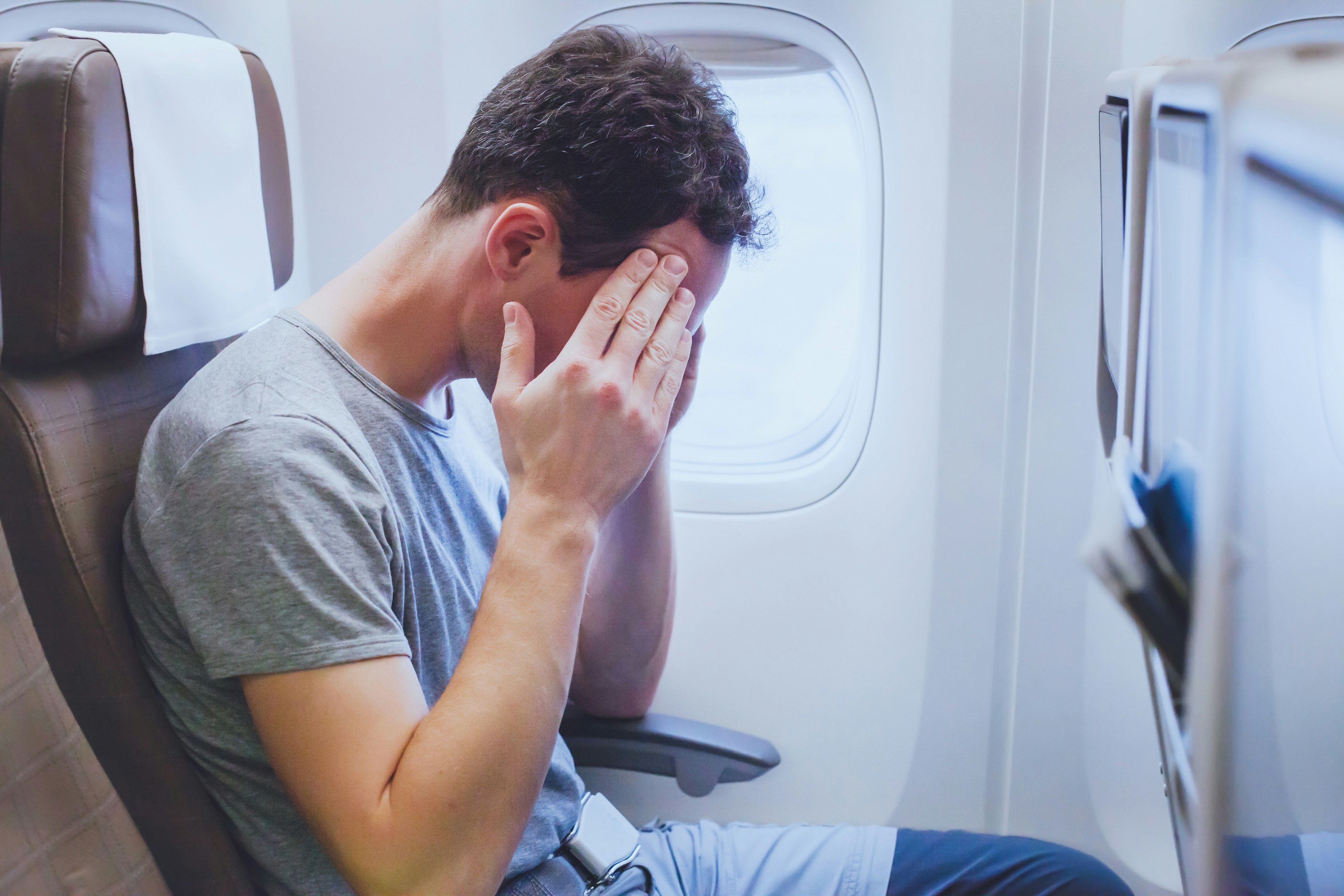 Man holding his head on the plane. Sunlight is coming through the window.