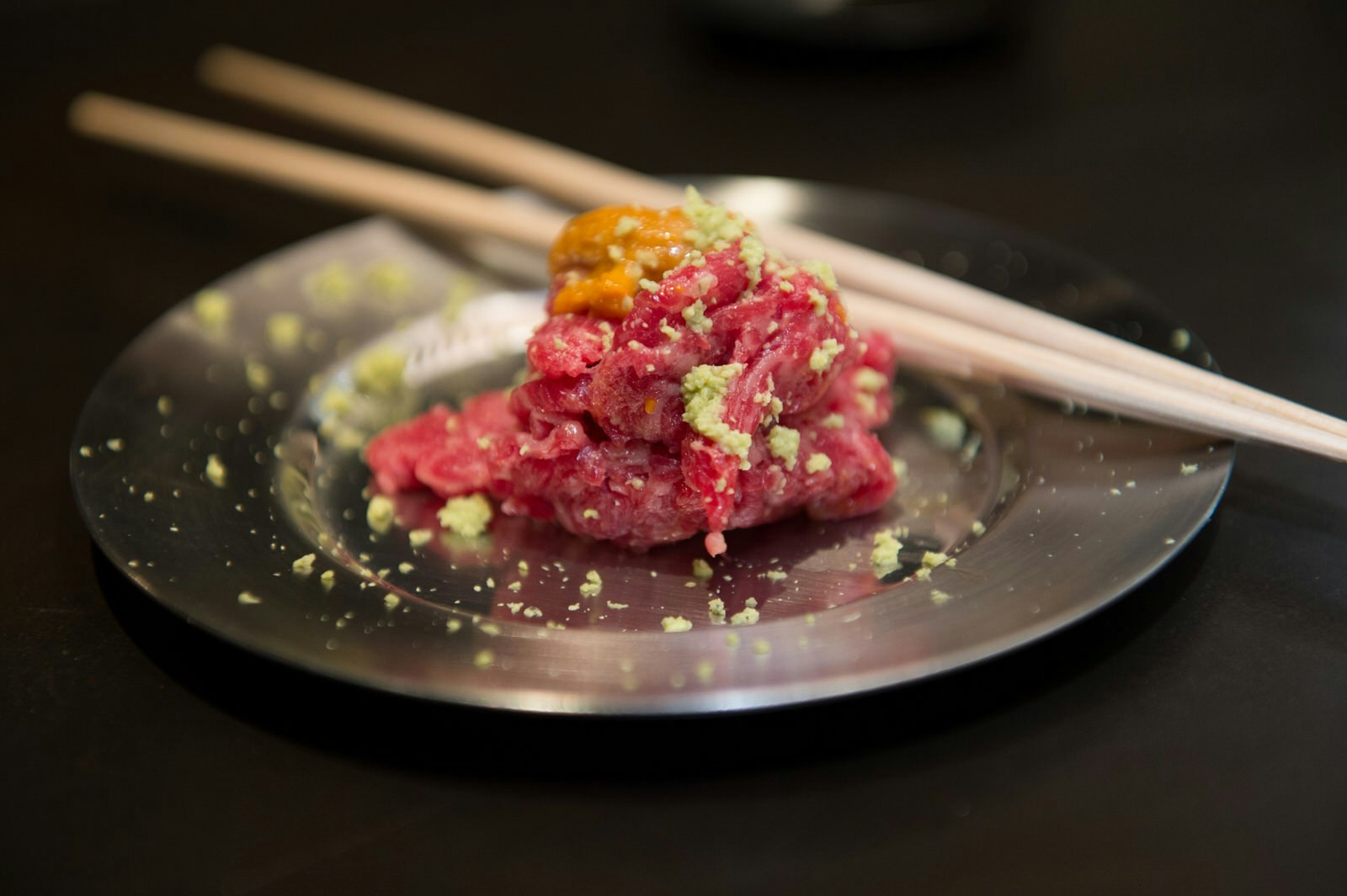 A view of a dish being served during a dinner with Masa Takayama at Masa restaurant in New York. The steak tartare is served on a stainless steel plate, with a sprinkle of wasabi alongside some chopsticks