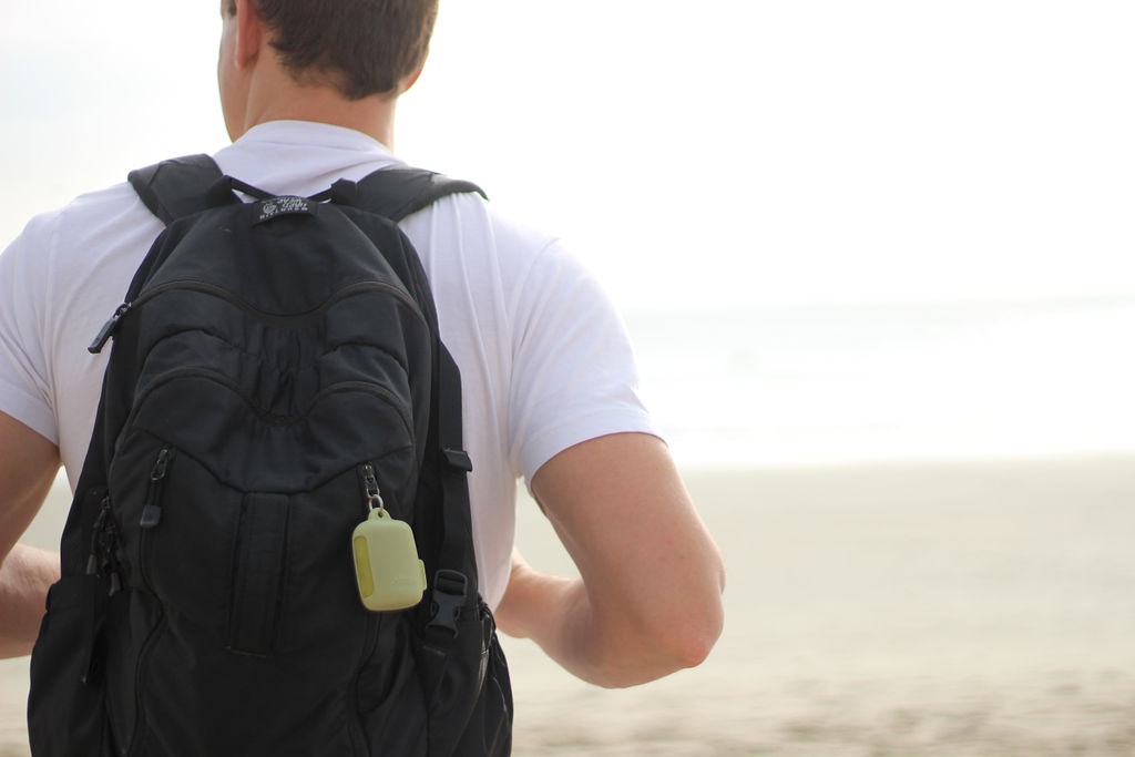 A man in a white tee and a black backpack with a yellow NanoDry hand towel attached, seen from behind