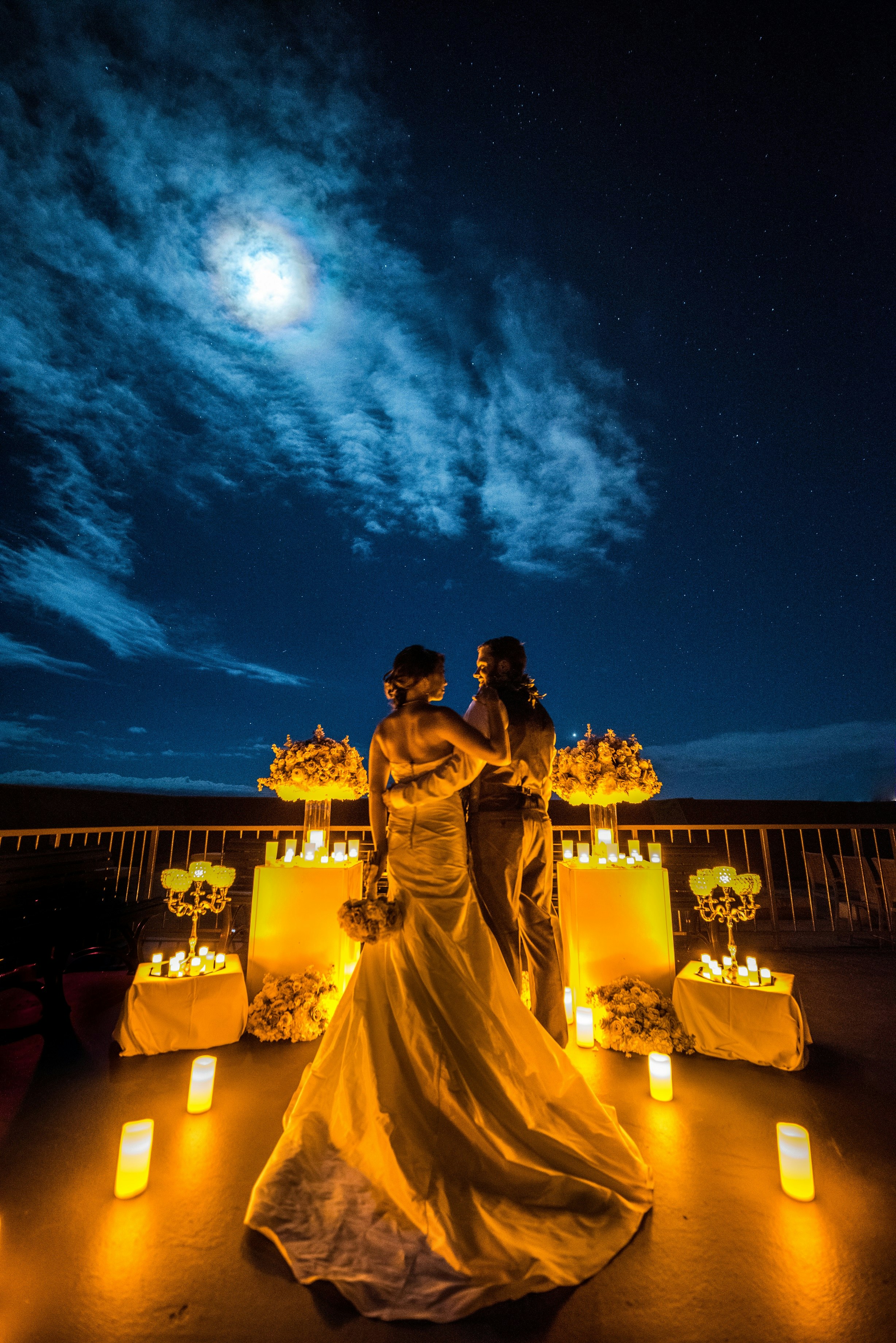 Bridal couple surrounded by candles and flowers under a full moon.jpg