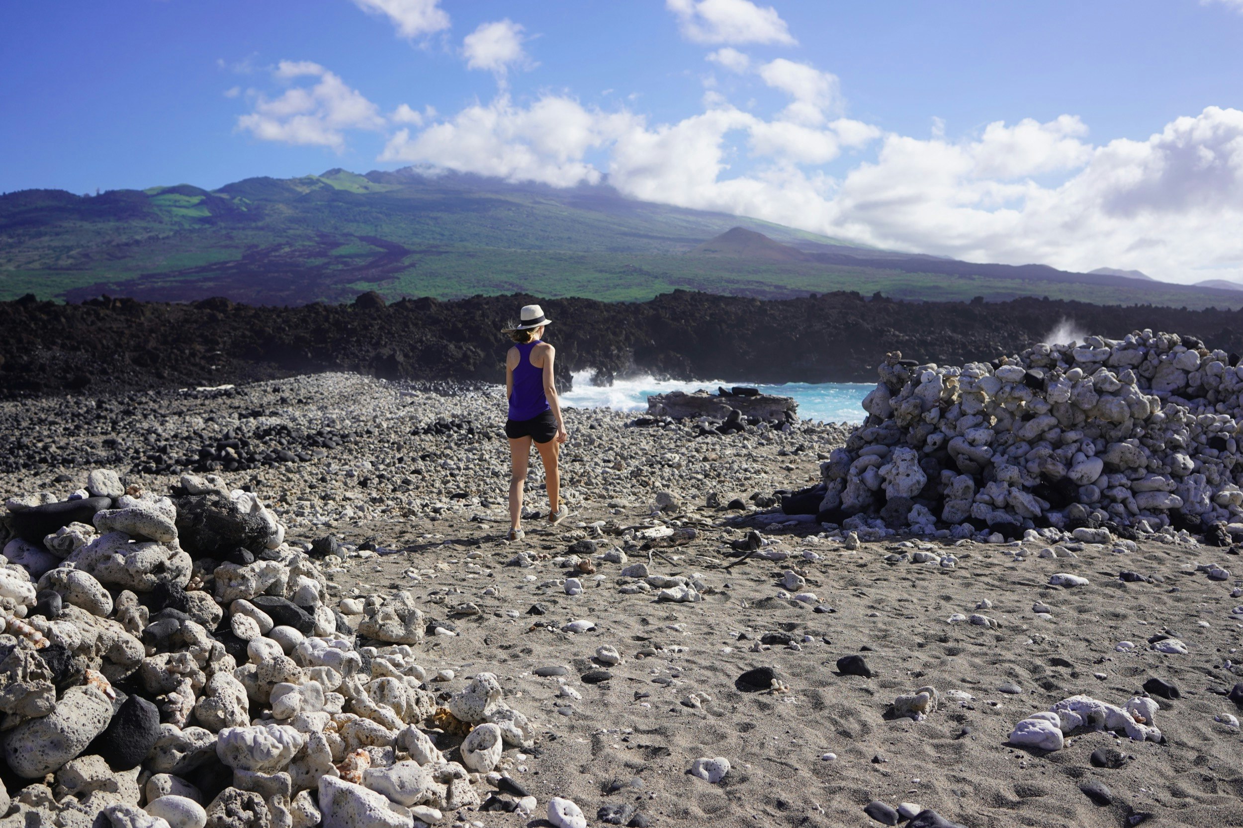 A woman walks along a black beach with bleached white rocks in Hawaii; Maui sites without tourists