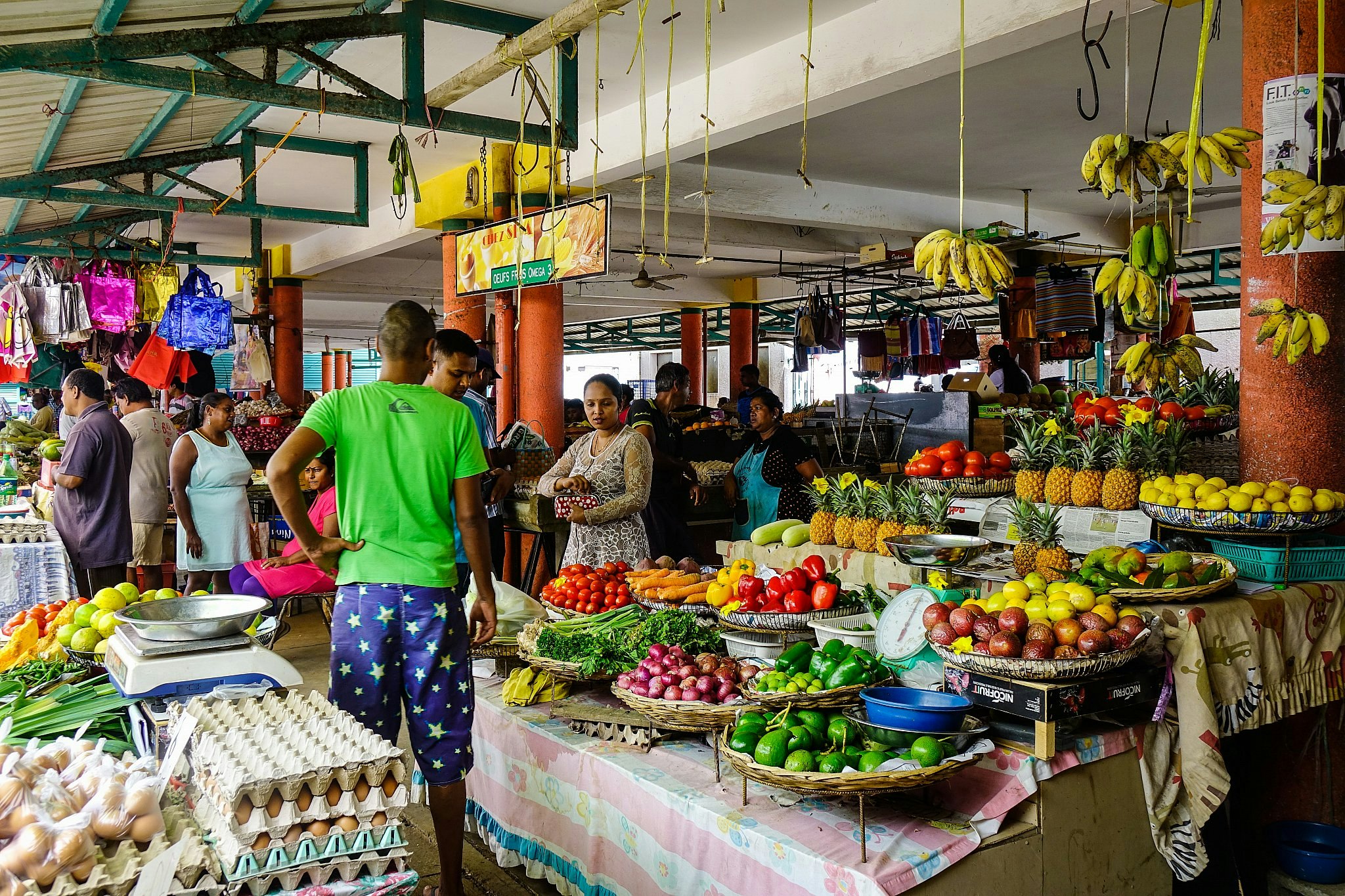 A Mauritius market, with people by a stall laden with colourful fresh produce.