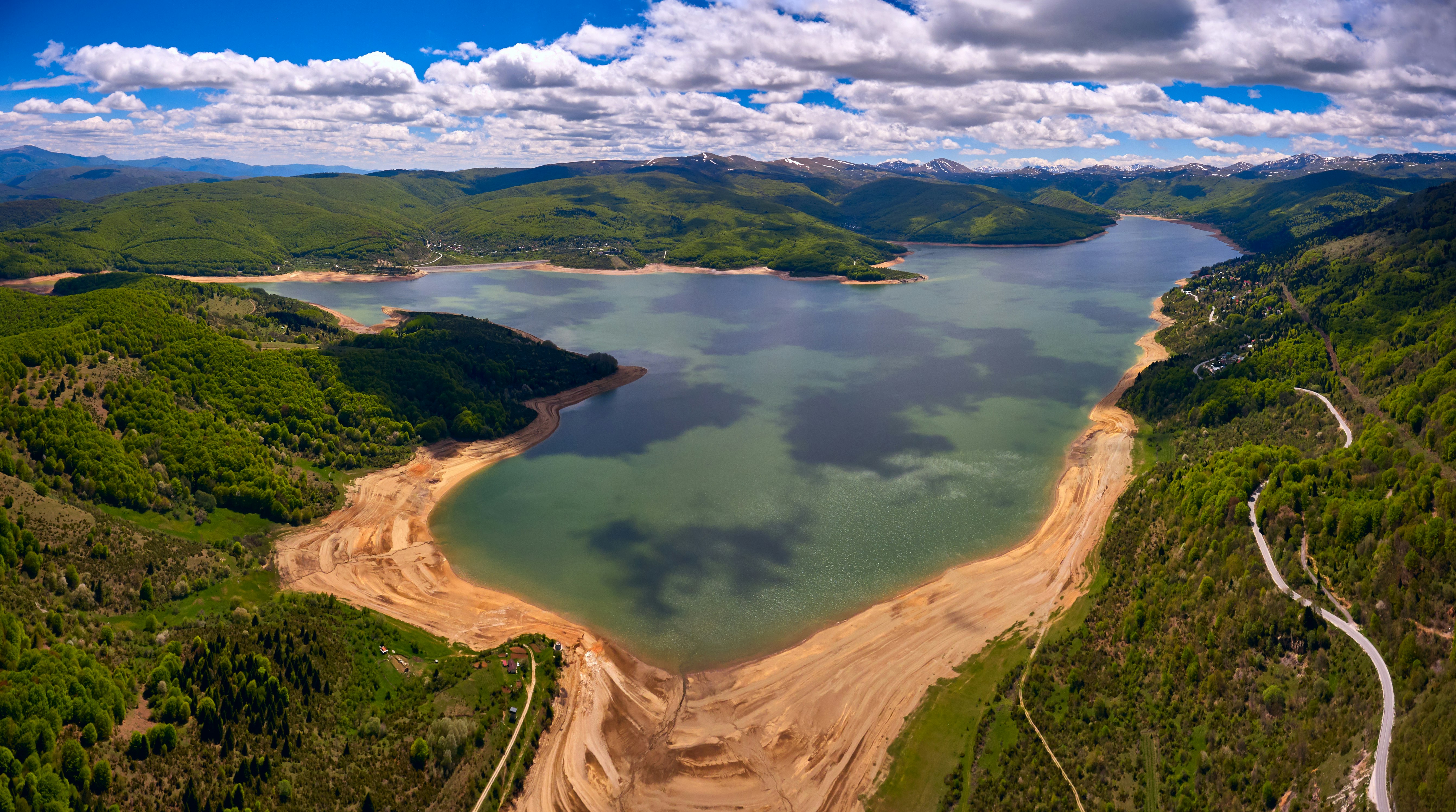 Aerial view of Lake Lake Mavrovo surrounded by light-brown sand and thick green forests; Best in Travel North Macedonia 