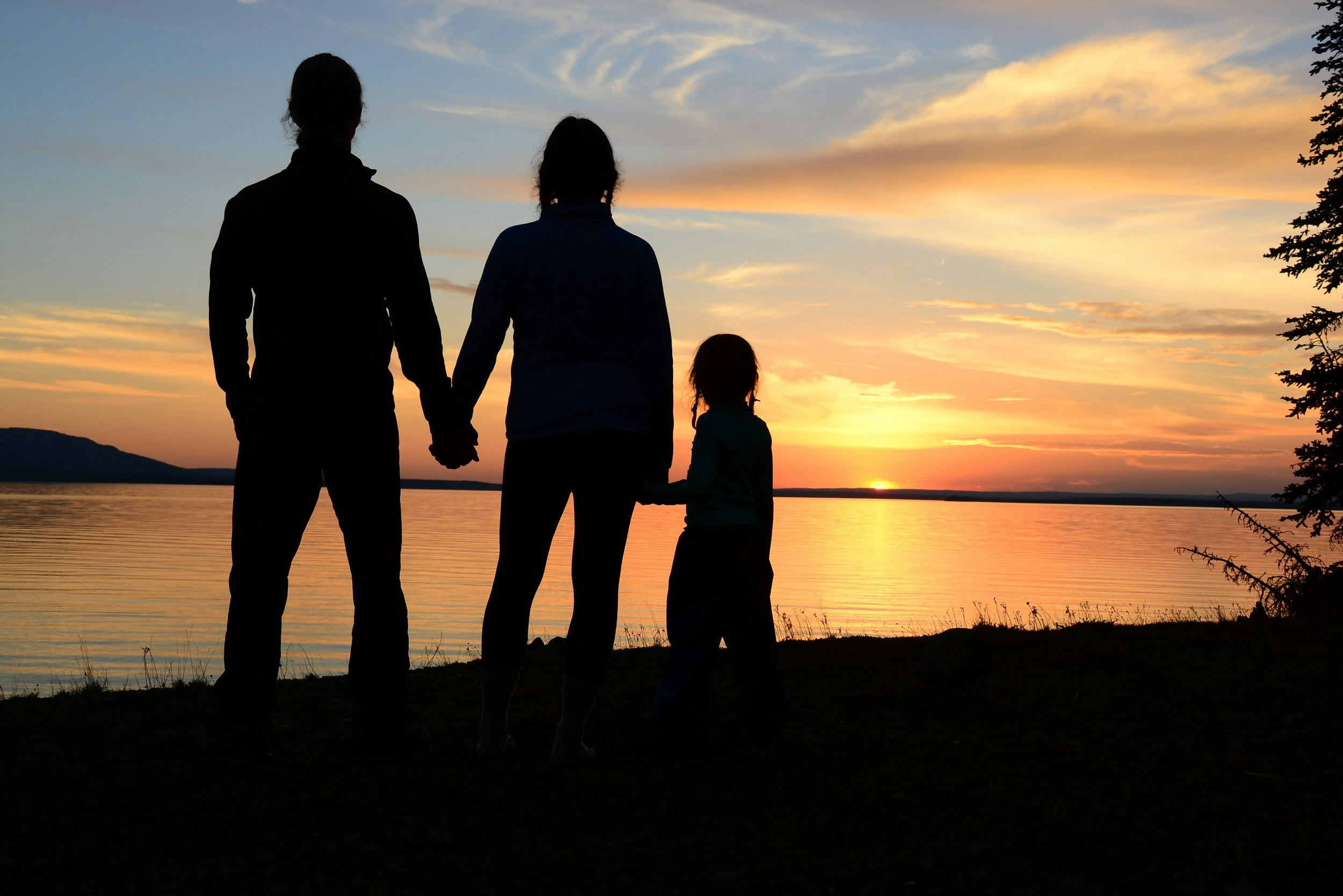 A man and a woman and their small daughter are silhouetted against a sunset as it is reflected in the surface of a lake; Project Remote