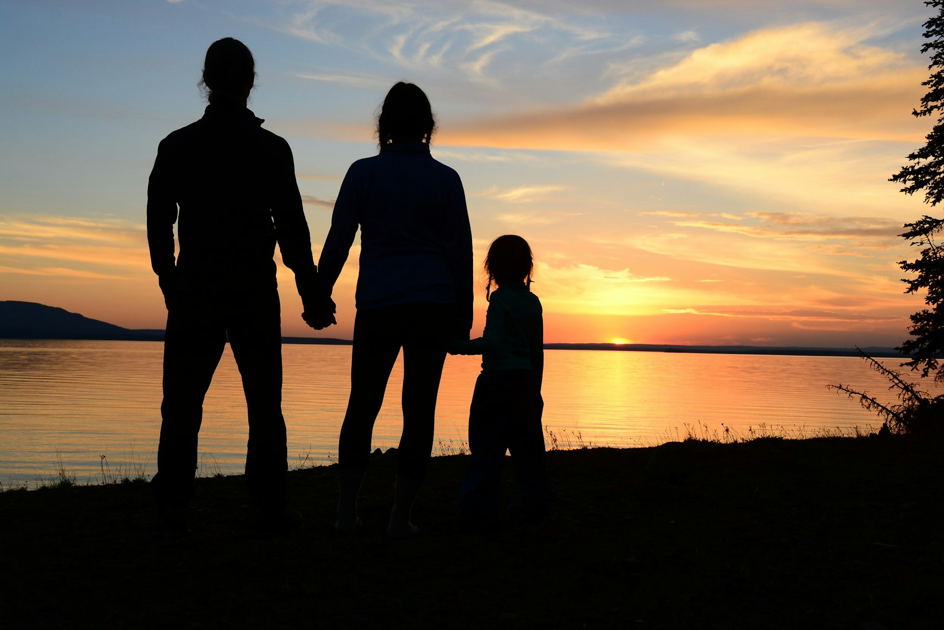 A man and a woman and their small daughter are silhouetted against a sunset as it is reflected in the surface of a lake; Project Remote