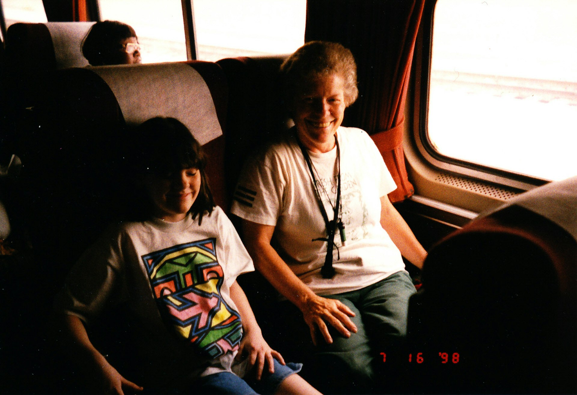 Meghan as a teenager and her grandmother smile at the camera sitting in an Amtrak train carriage
