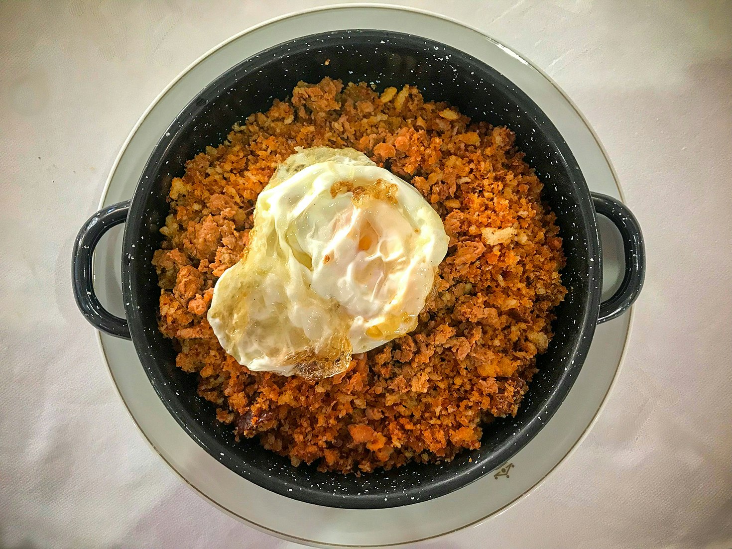 A black serving dish with handles, seen from above, is filled with a fine, lightly spiced, orange-coloured mixture and topped with a fried egg, a traditional dish known as migas trashumanica in Zamora, Spain