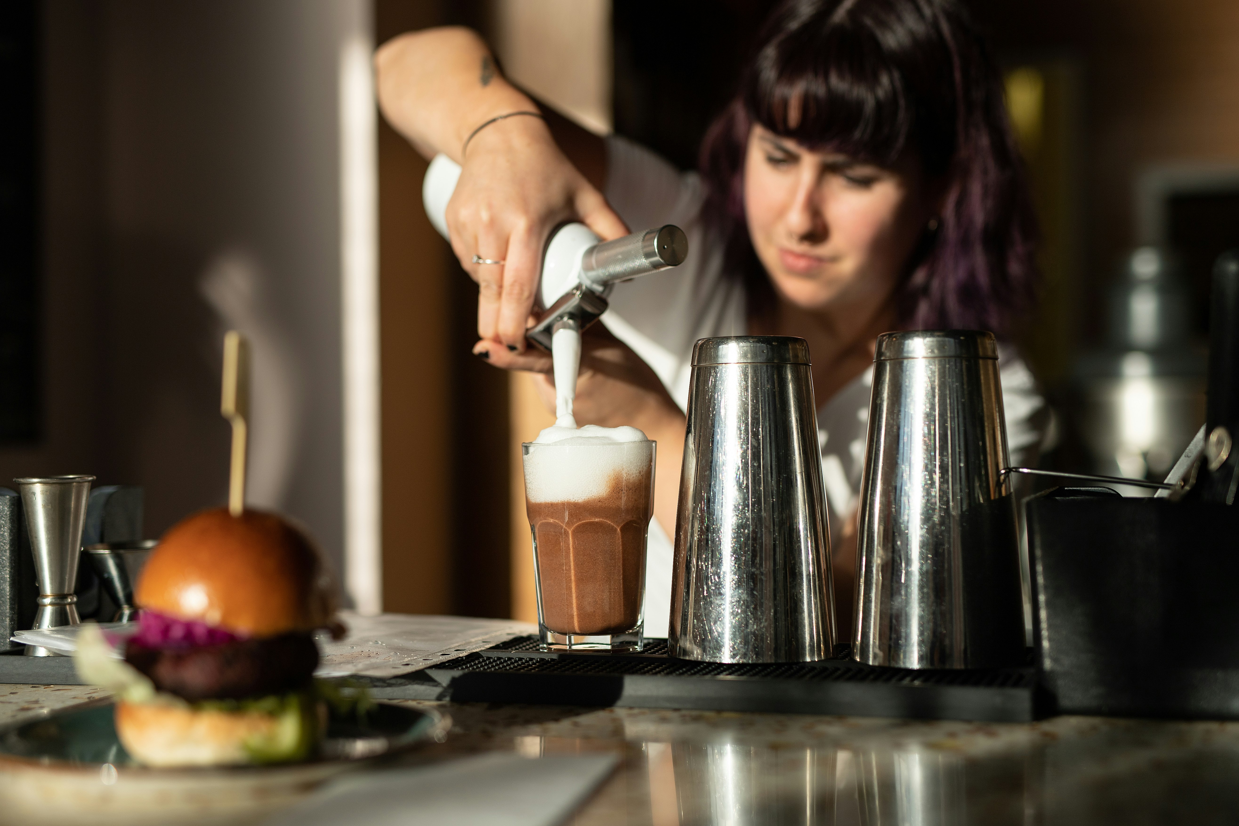 A woman with dark hair concentrates as she pipes foam onto a dark, chocolatey drink at vegan restaurant Mildred's in London, United Kingdom