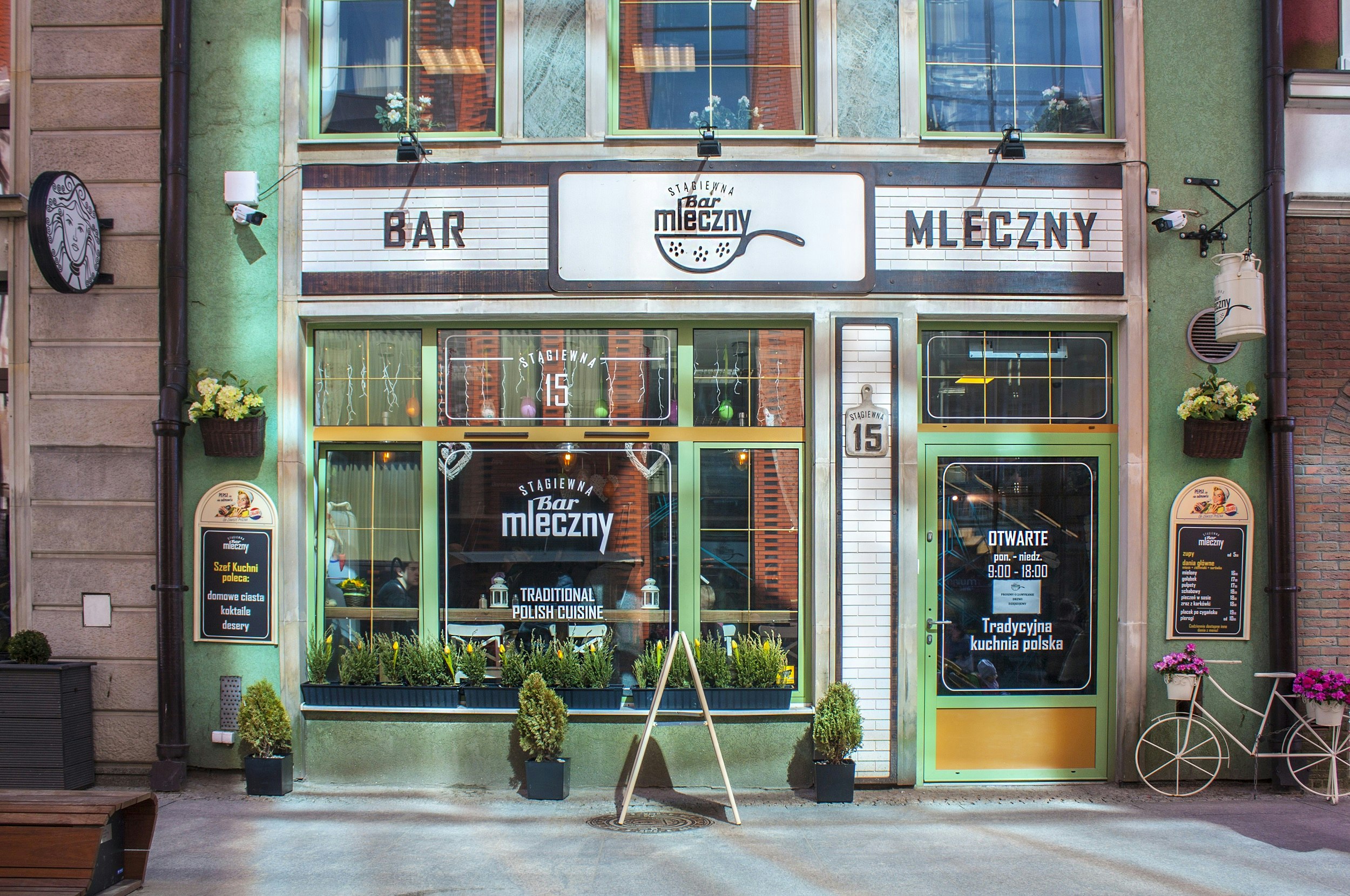 Front of a restaurant with green-framed windows. There's a large sign in black-and-white above the windows that says 'Bar Mleckzny'