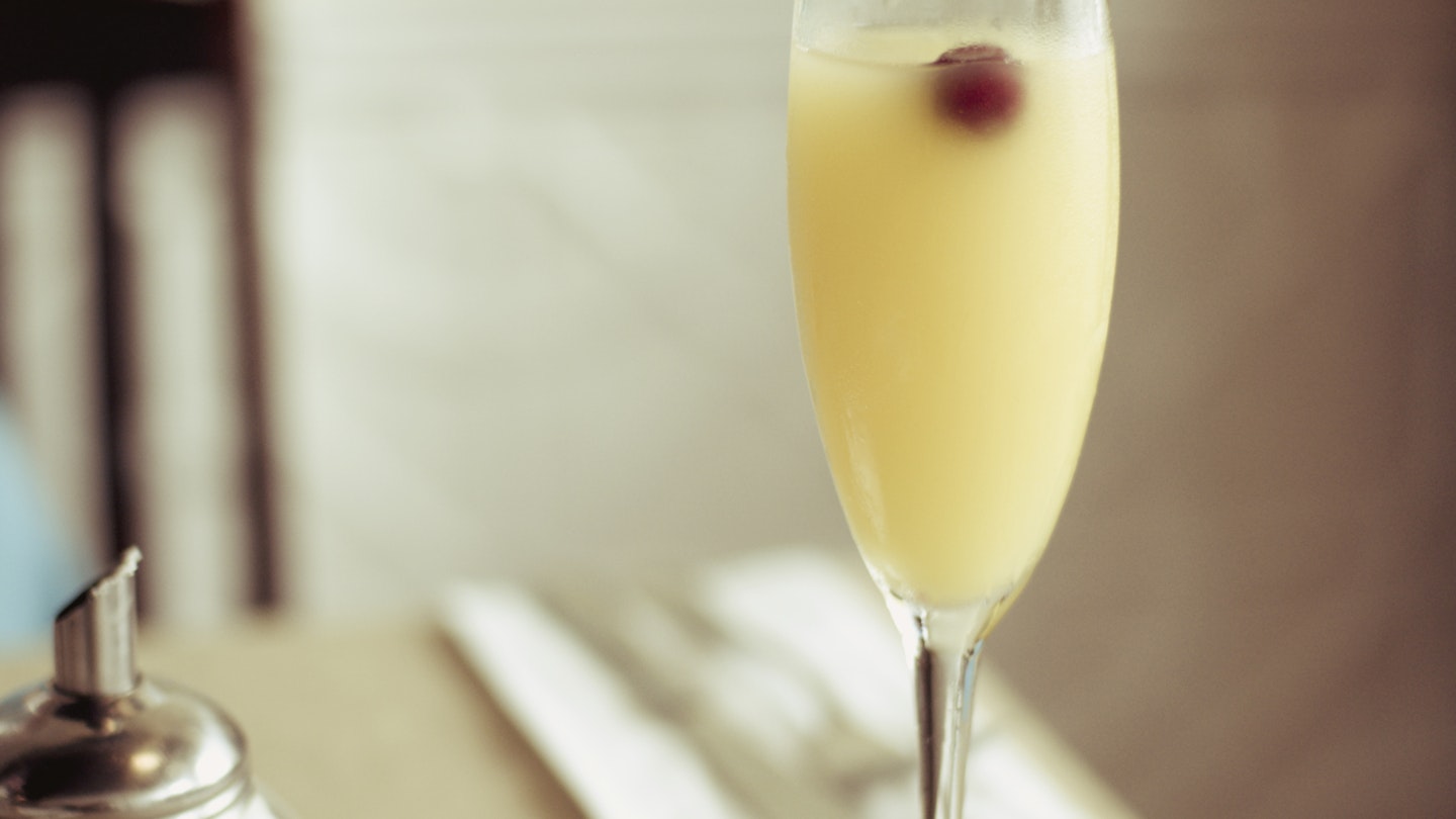 A wine glass filled with mimosa made with orange juice, Grand Marnier and champagne and topped with a cherry