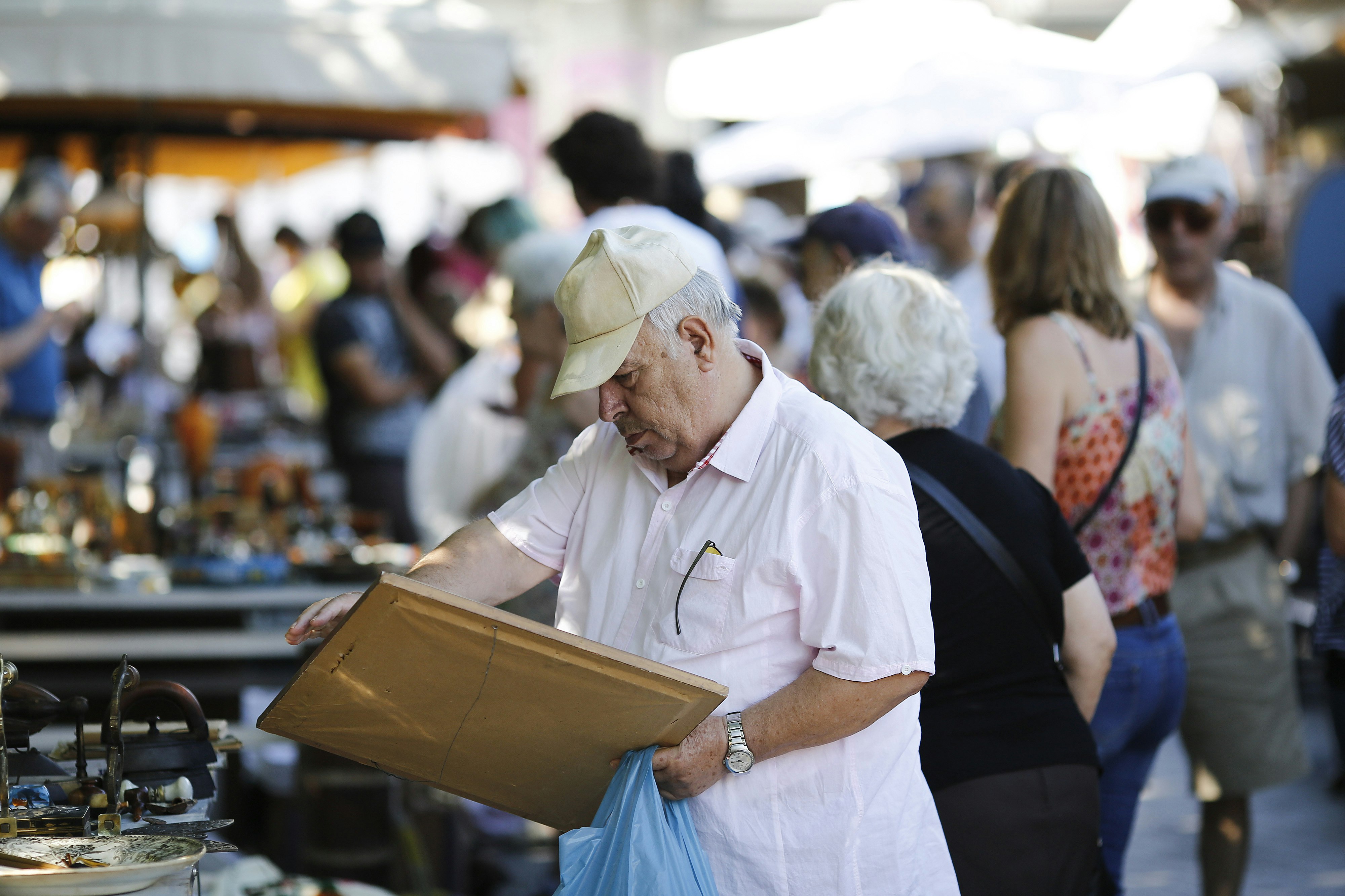 A man surrounded by other shoppers looks at a framed picture in the midst of Monastiraki Flea Market in Athens, Greece