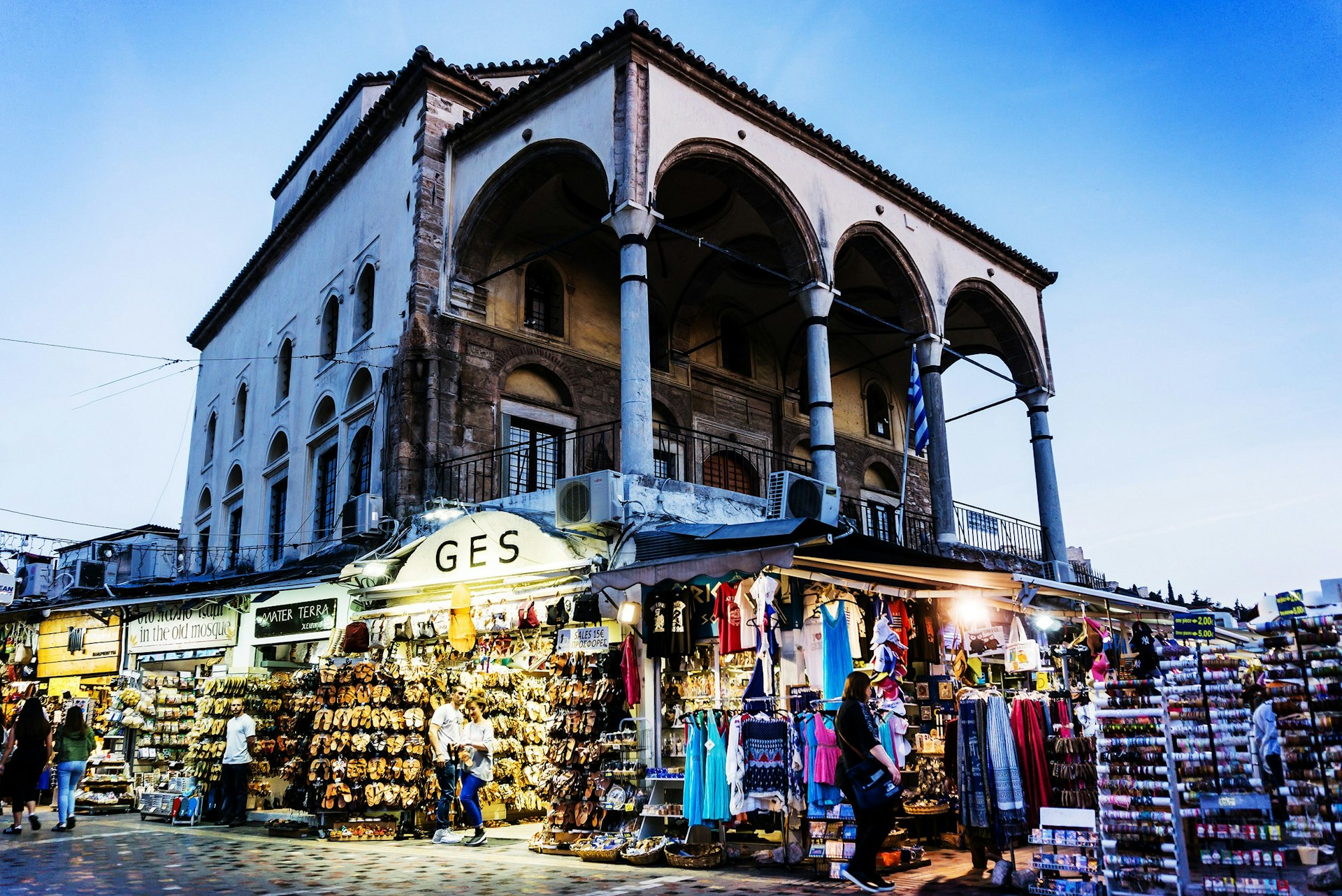 A large building, with four columns supporting its roof, is surrounded by stalls selling clothes, shoes and souvenirs