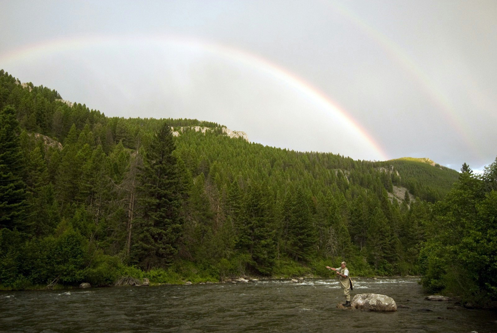A rainbow arcs over an angler as he fly fishes on a river in Montana; World's best rivers for fly fishing