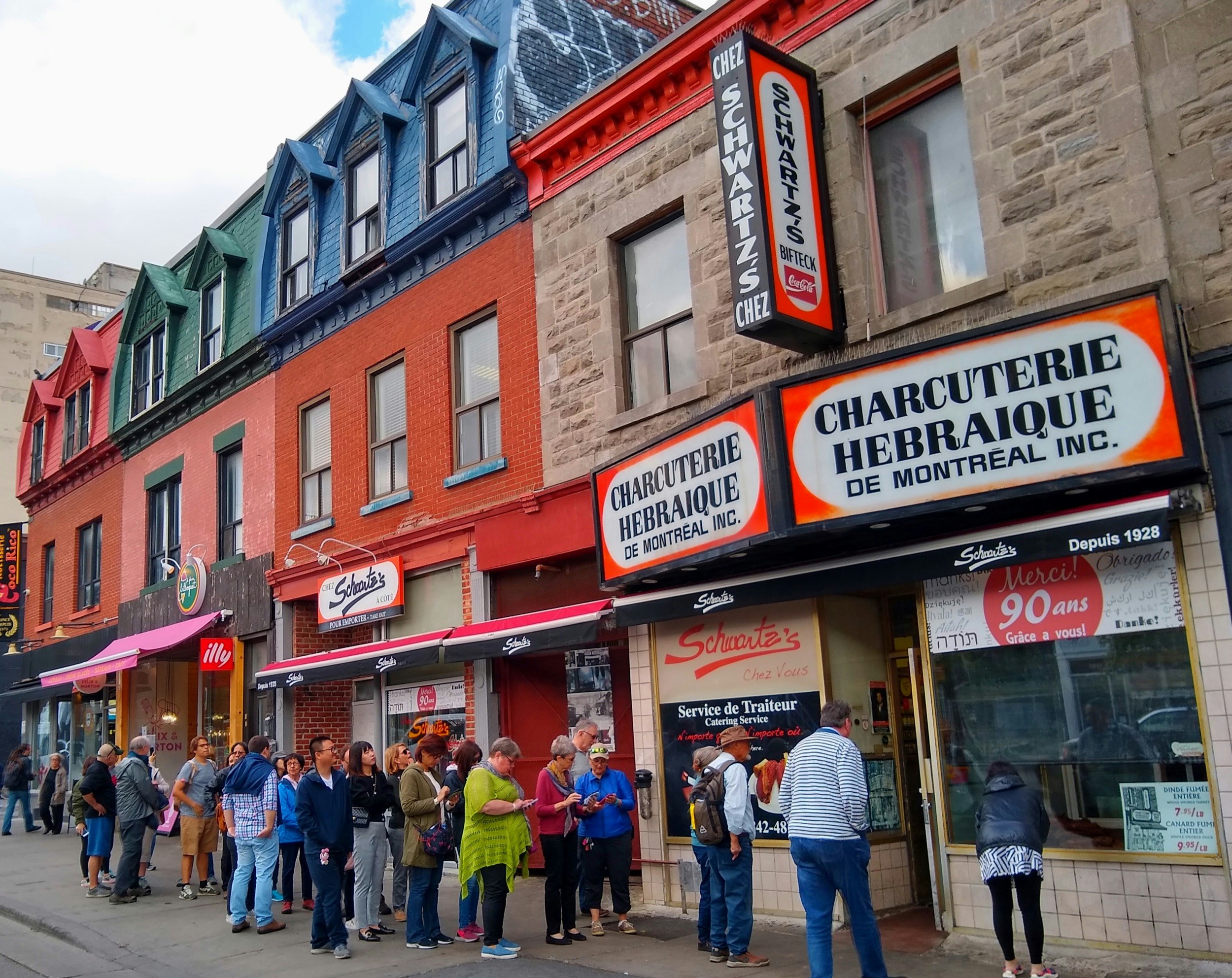 A line of people waits at the door to a red-roofed deli in downtown. It's obviously chilly outside; Fall in Montreal