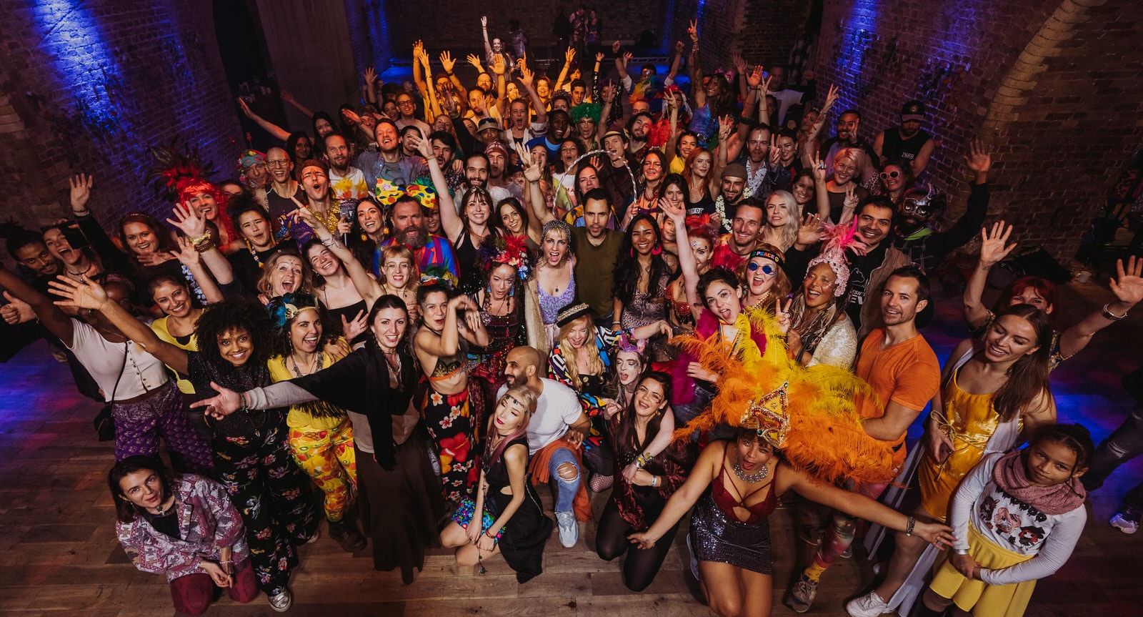 A large crowd of people dressed for a rave smiling and cheering at the camera during a Morning Gloryville event in London