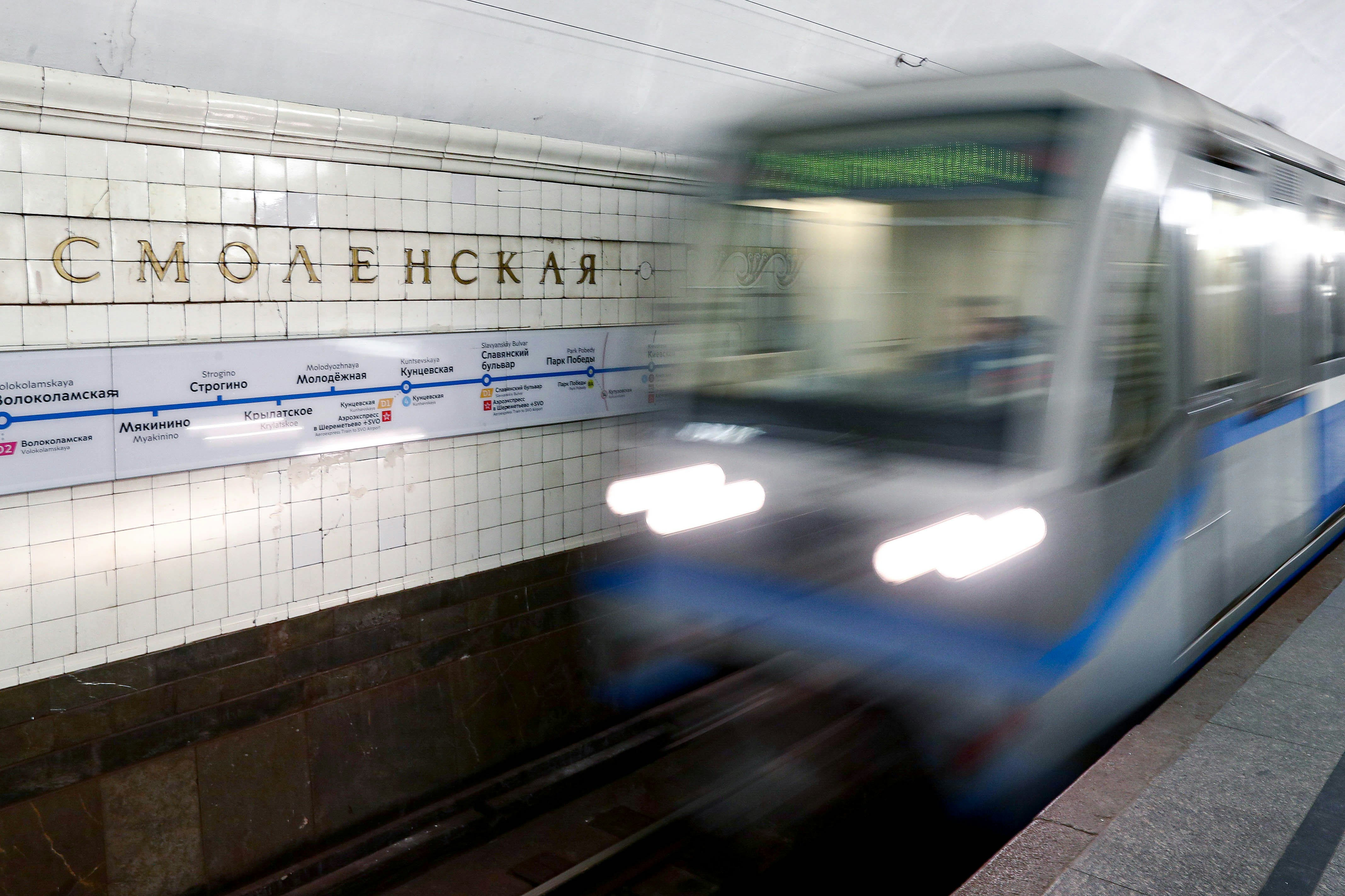 A blurred train travelling at speed through a station with a tiled wall and a station guide.