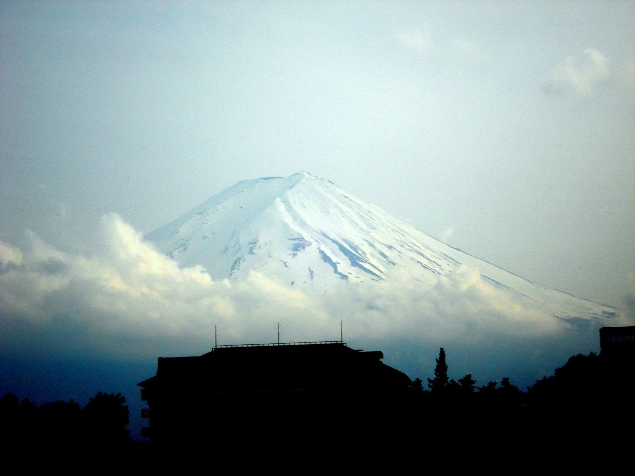 Clouds around the base of Mt Fuji, in Japan, with a building silhouetted in the foreground