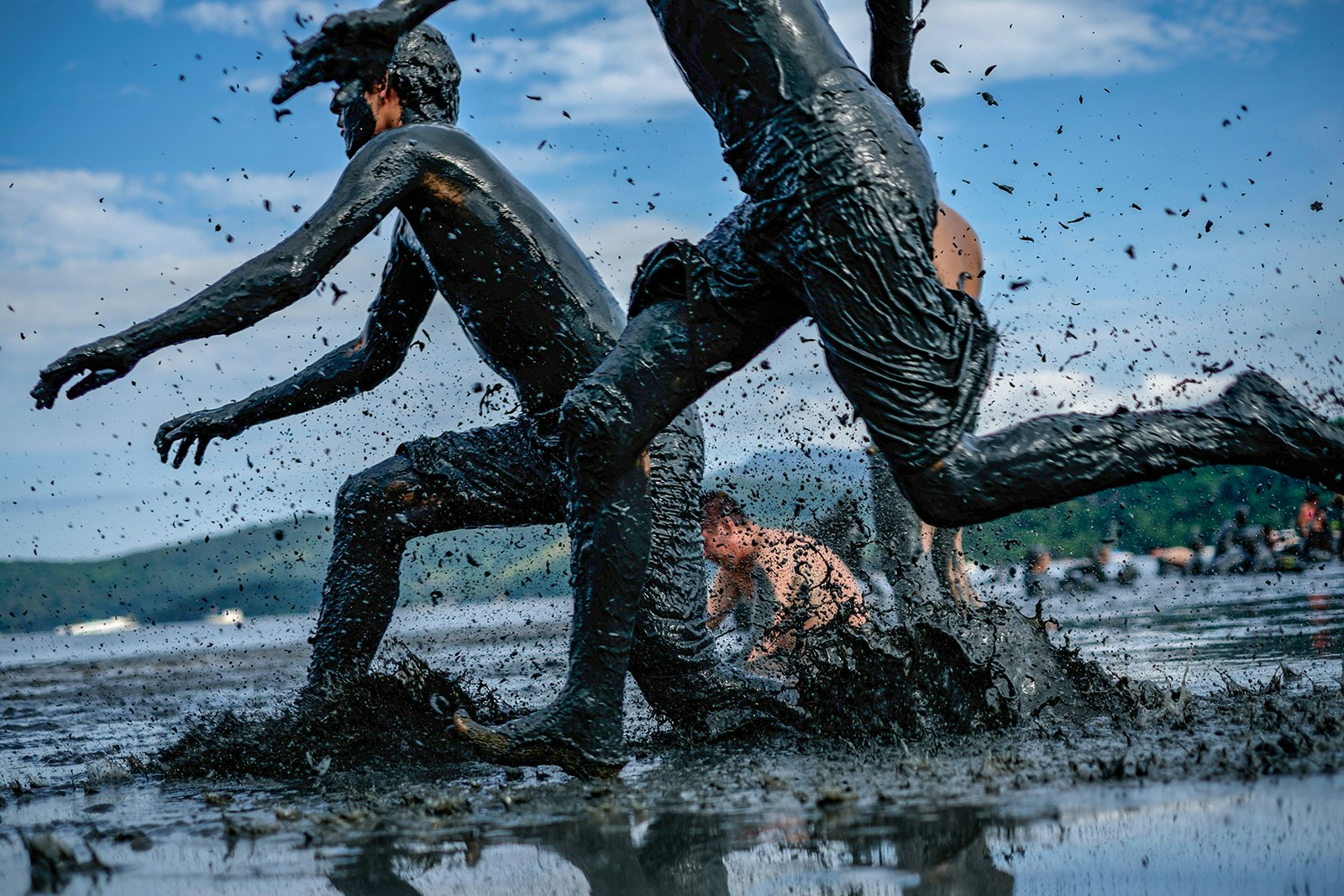 People splash through calf-deep black mud on the shores of Paraty