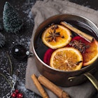 A silver pan filled with mulled wine, cinnamon sticks, orange slices and star anise is surrounded by miniature frosted Christmas trees, cranberries and an ornament