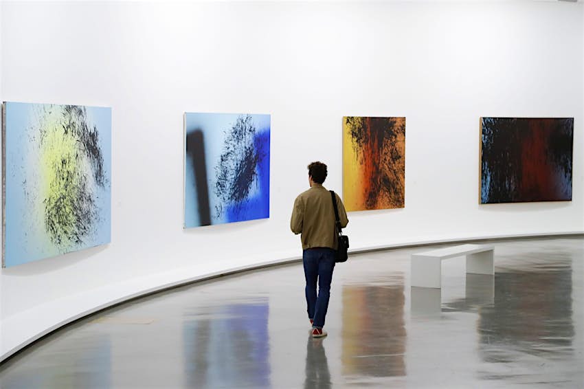 A man walks through a gallery containing white walls and colorful modern paintings