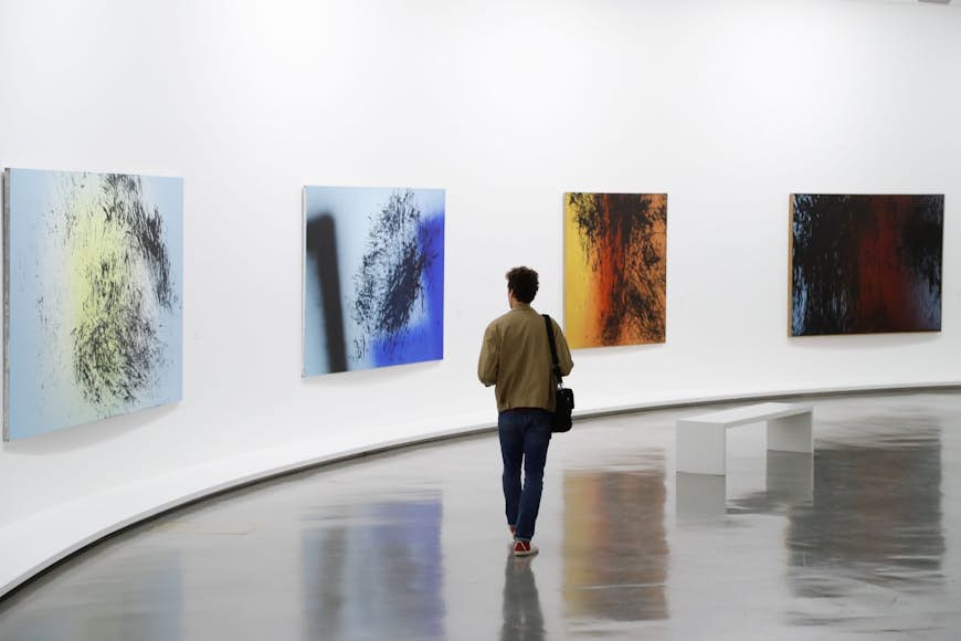 En man går genom ett galleri med vita väggar och färgglada moderna målningar