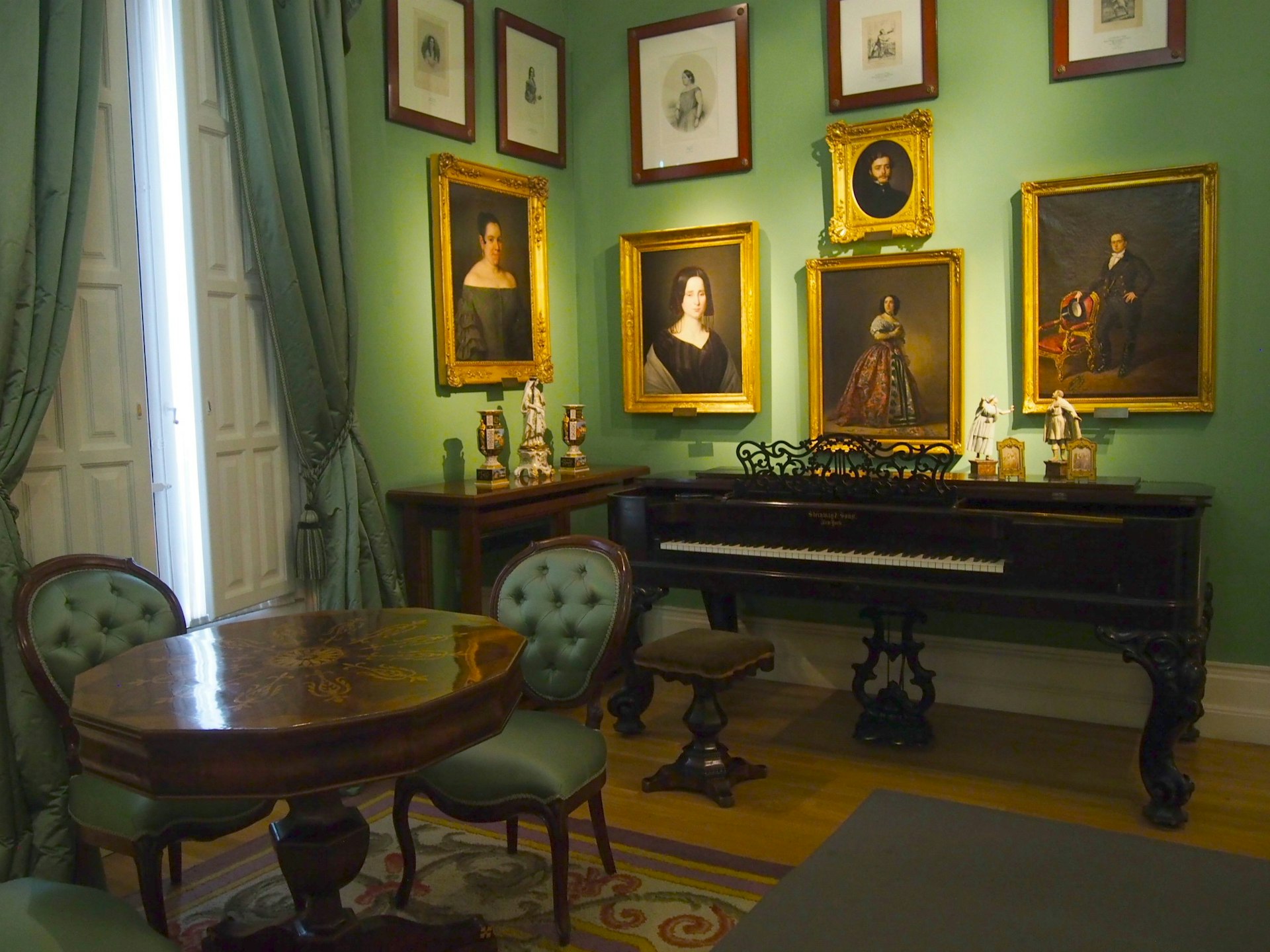A piano sits against the wall beneath paintings at the Museo del Romanticismo, Madrid.
