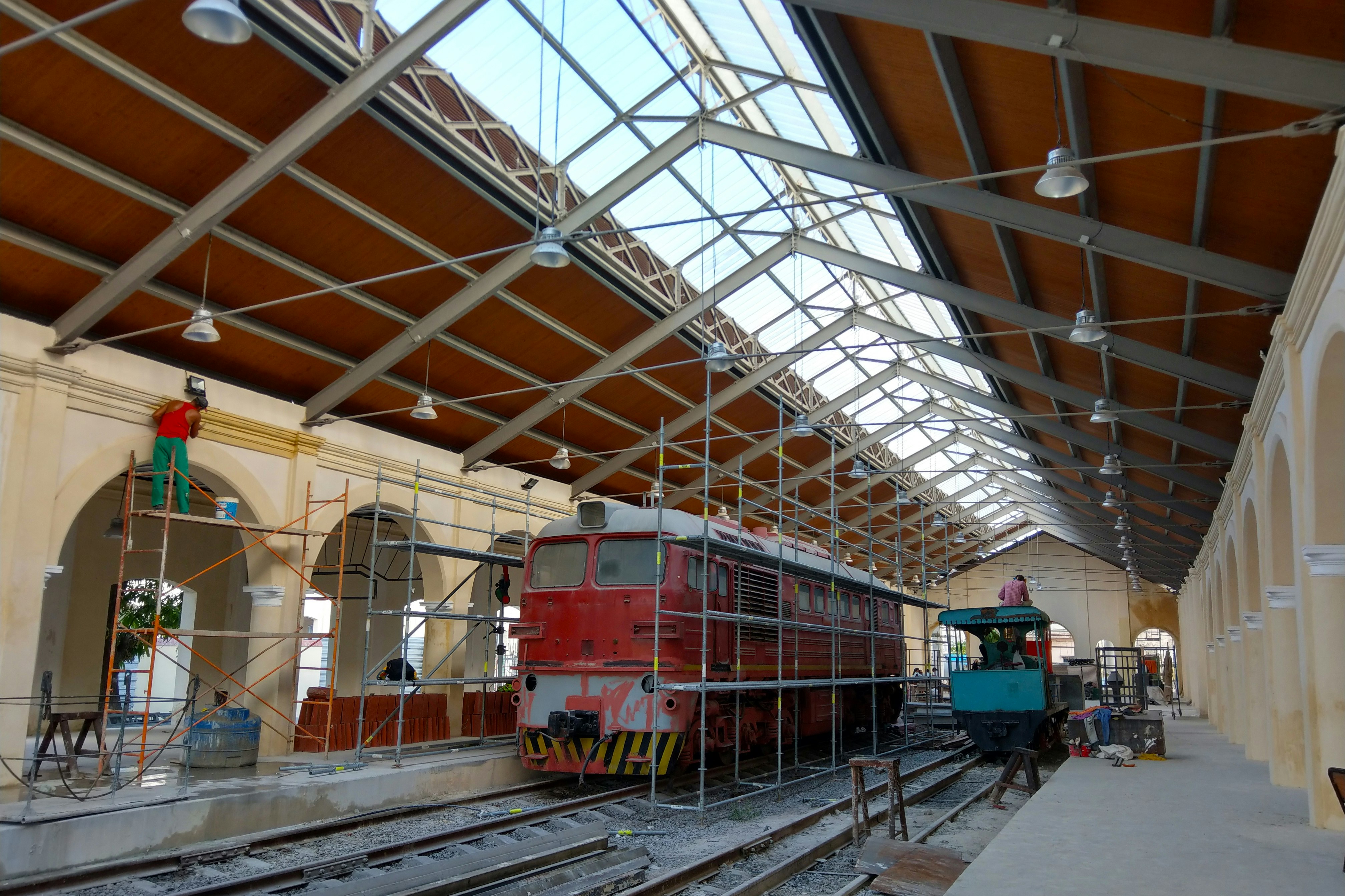 Scaffolding surrounds an old locomotives in an old train station in Havana, In the background, men work on the interior of the train station; Historic Havana sites 