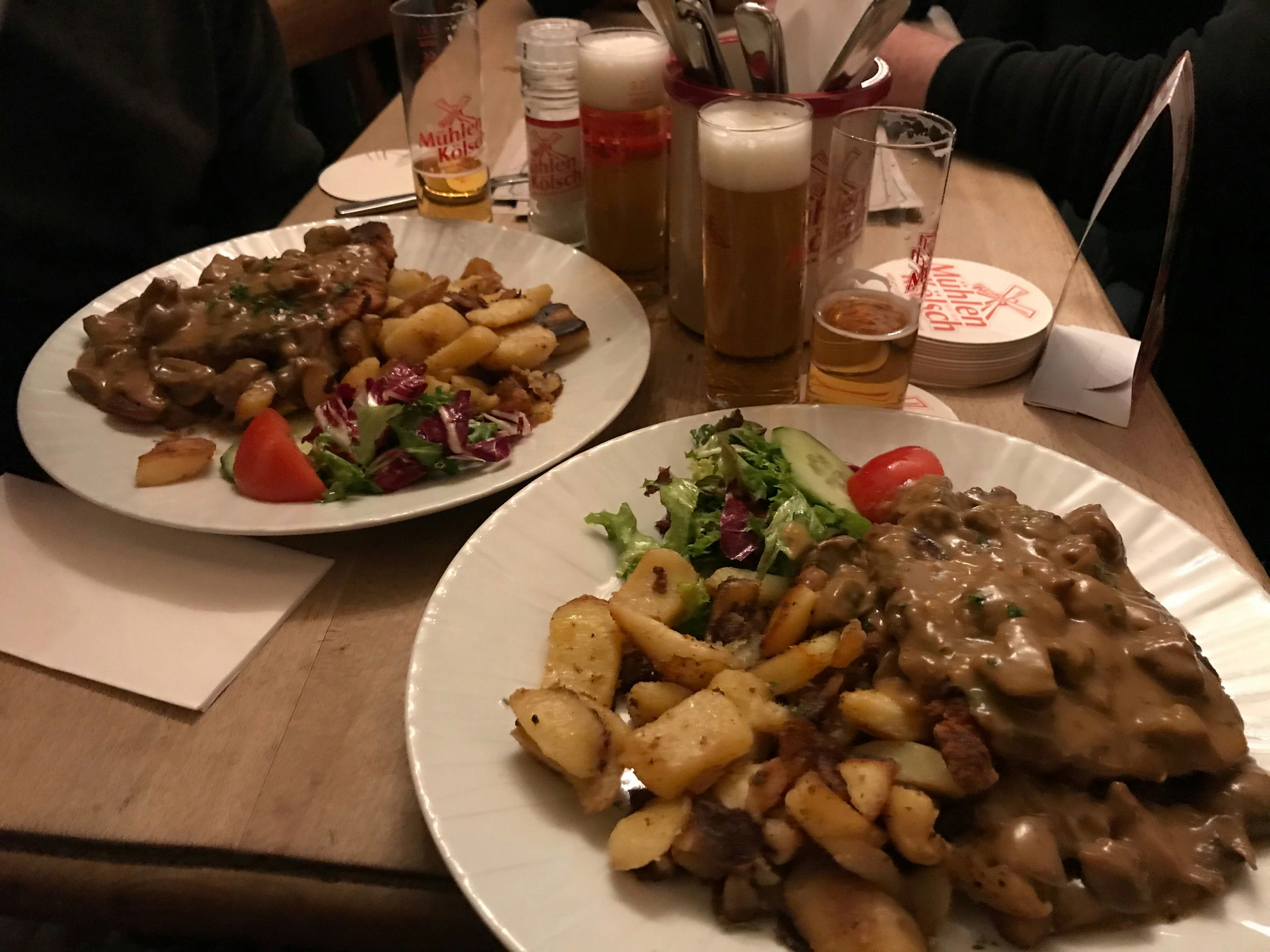 Two plates of mushroom schnitzel with fried potato and small glasses of beer on a wooden table.JPG