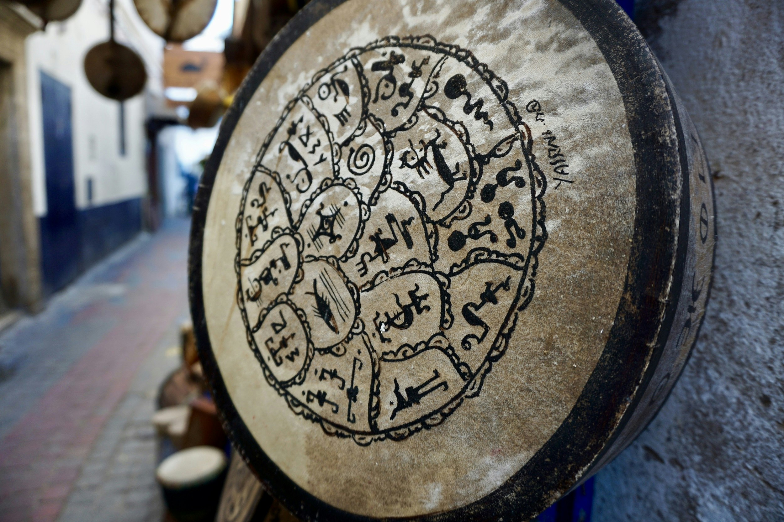 A shallow drum - covered in Berber writing and symbols - hangs on the wall of a music shop in an alleyway of Essaouira.