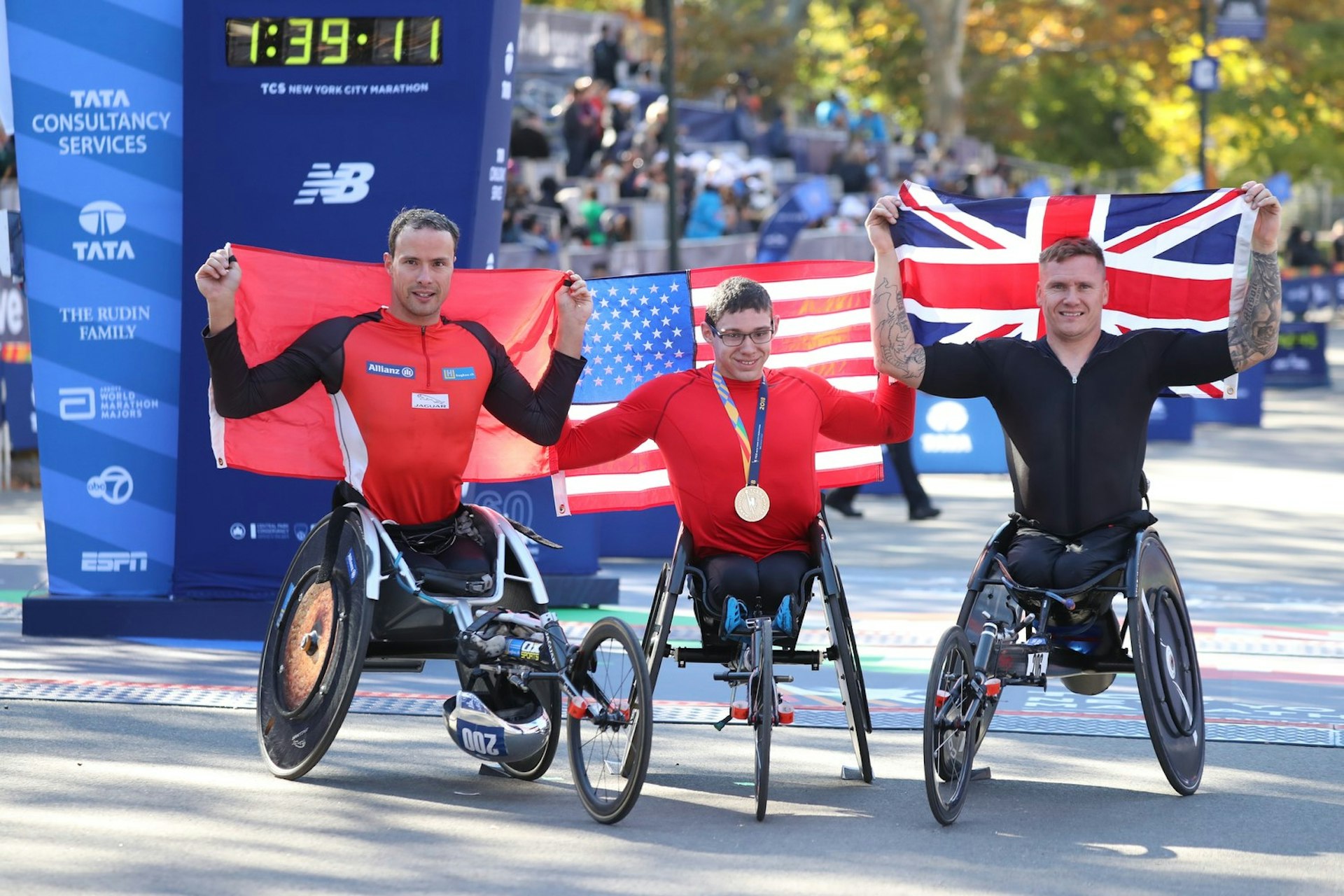 A trio of men in wheelchairs hold up flags of their respective countries after finishing the New York City Marathon