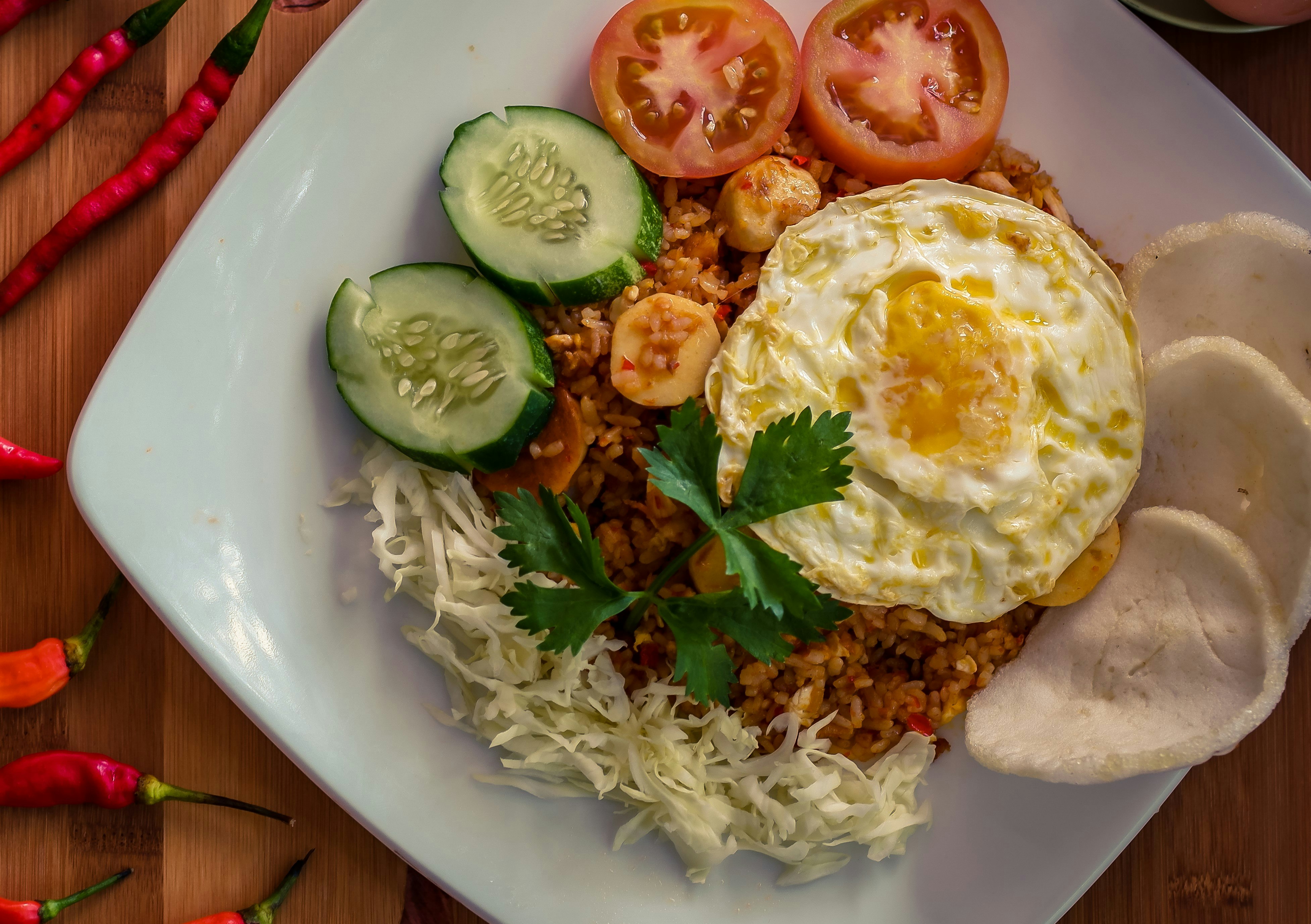 A top-down view of a plate of nasi goreng on a tabletop. The dish consists of rice and vegetables, with a fried egg placed on top.