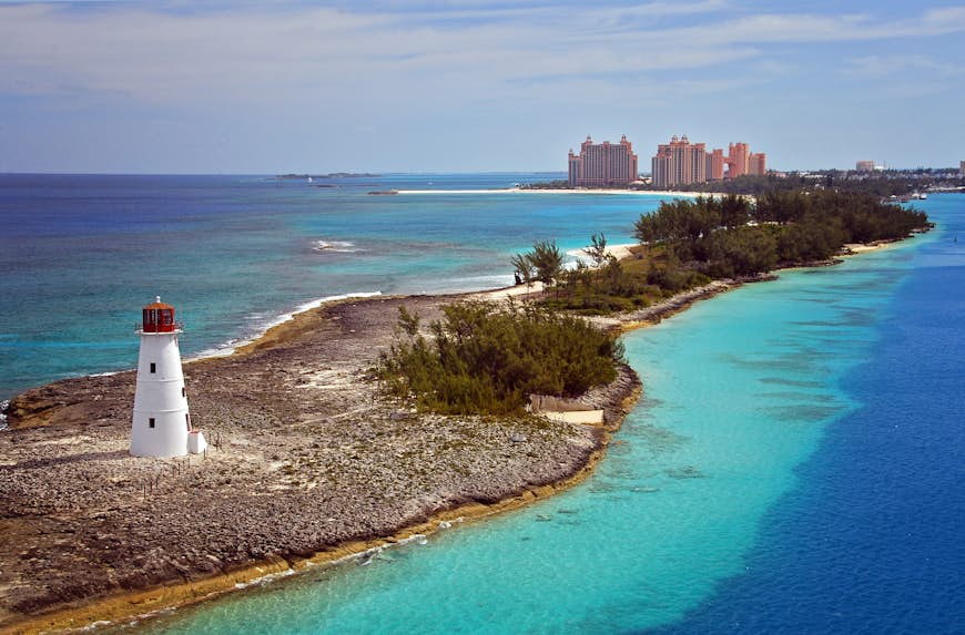 Aerial view of a light house on a rugged shore with overgrown bush. In the distance you can see the Atlantis Resort. 