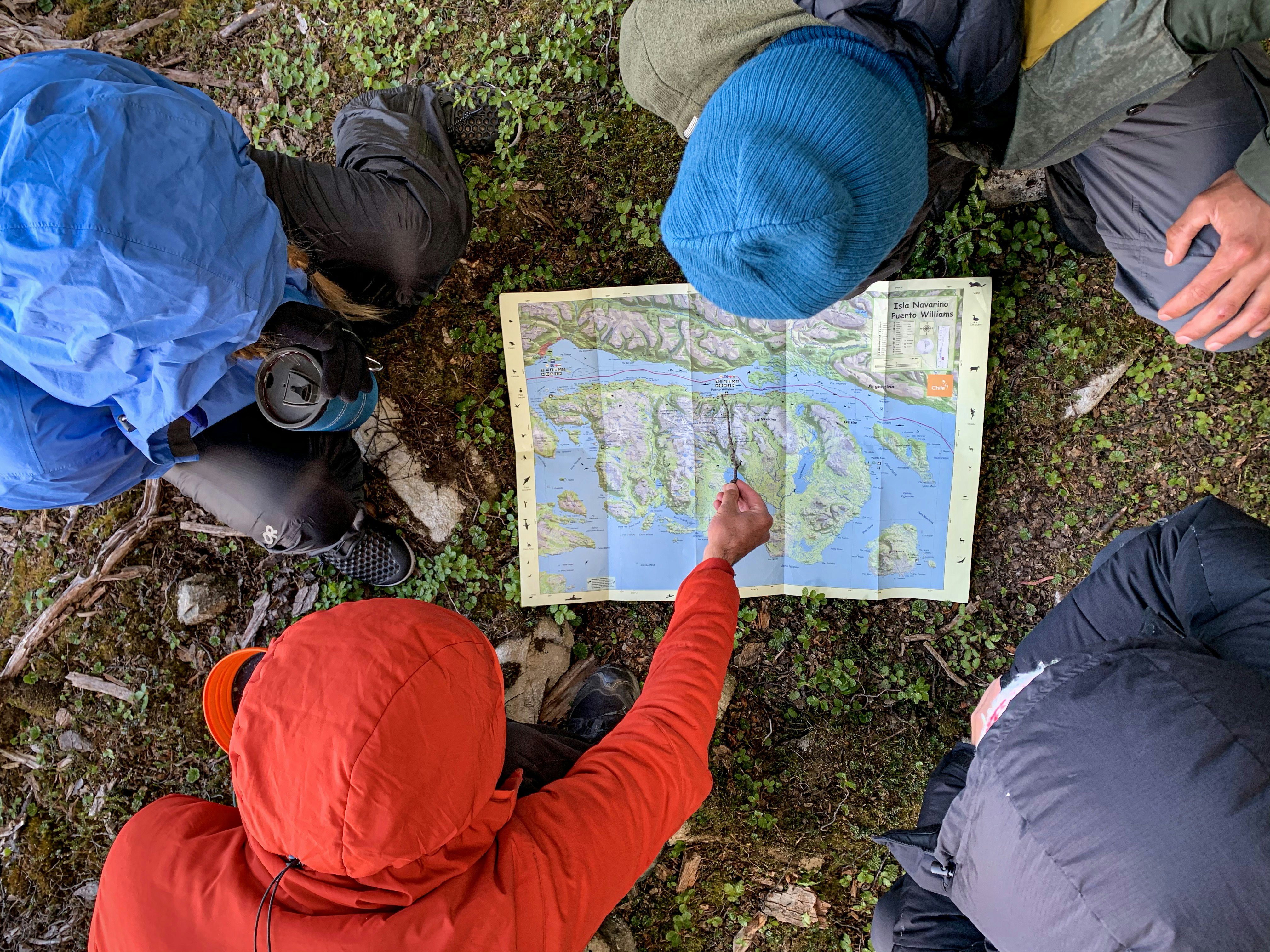Looking down on a group of four hikers who are planning their route on a paper map that's been laid on the ground.