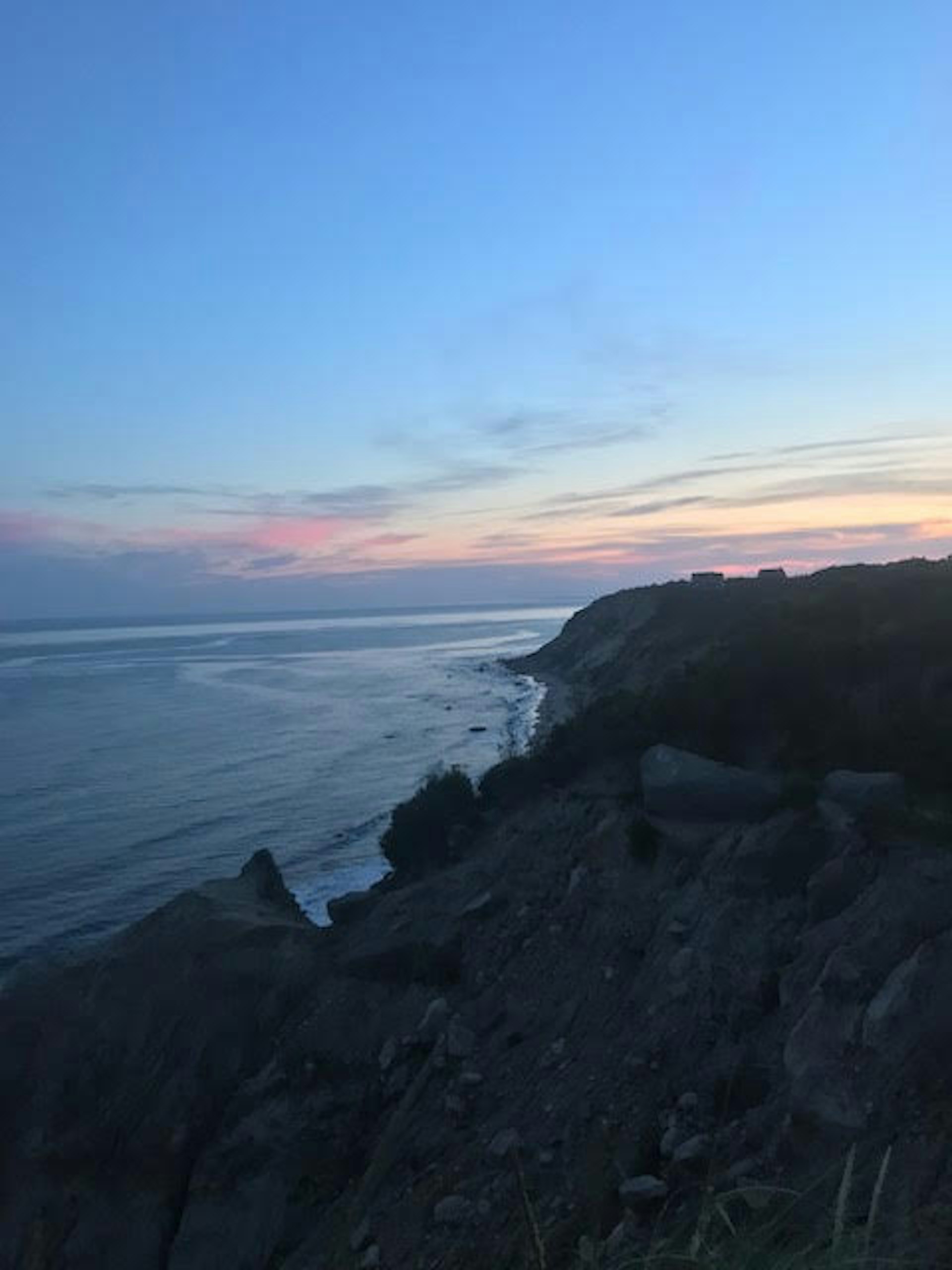 A rocky New England beach, on Block Island, at dusk. The outline of houses is visible in the distance.