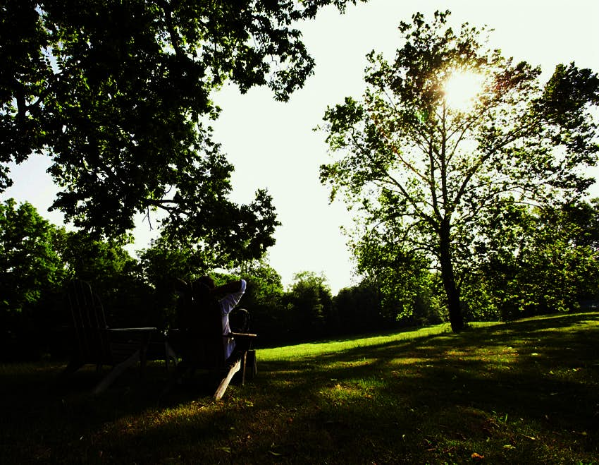 A man relaxes in a wooden chair on a grassy lawn