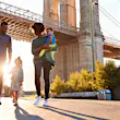 A family of four walks through the park under the Brooklyn Bridge