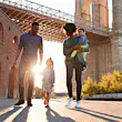 A family of four walks through the park under the Brooklyn Bridge