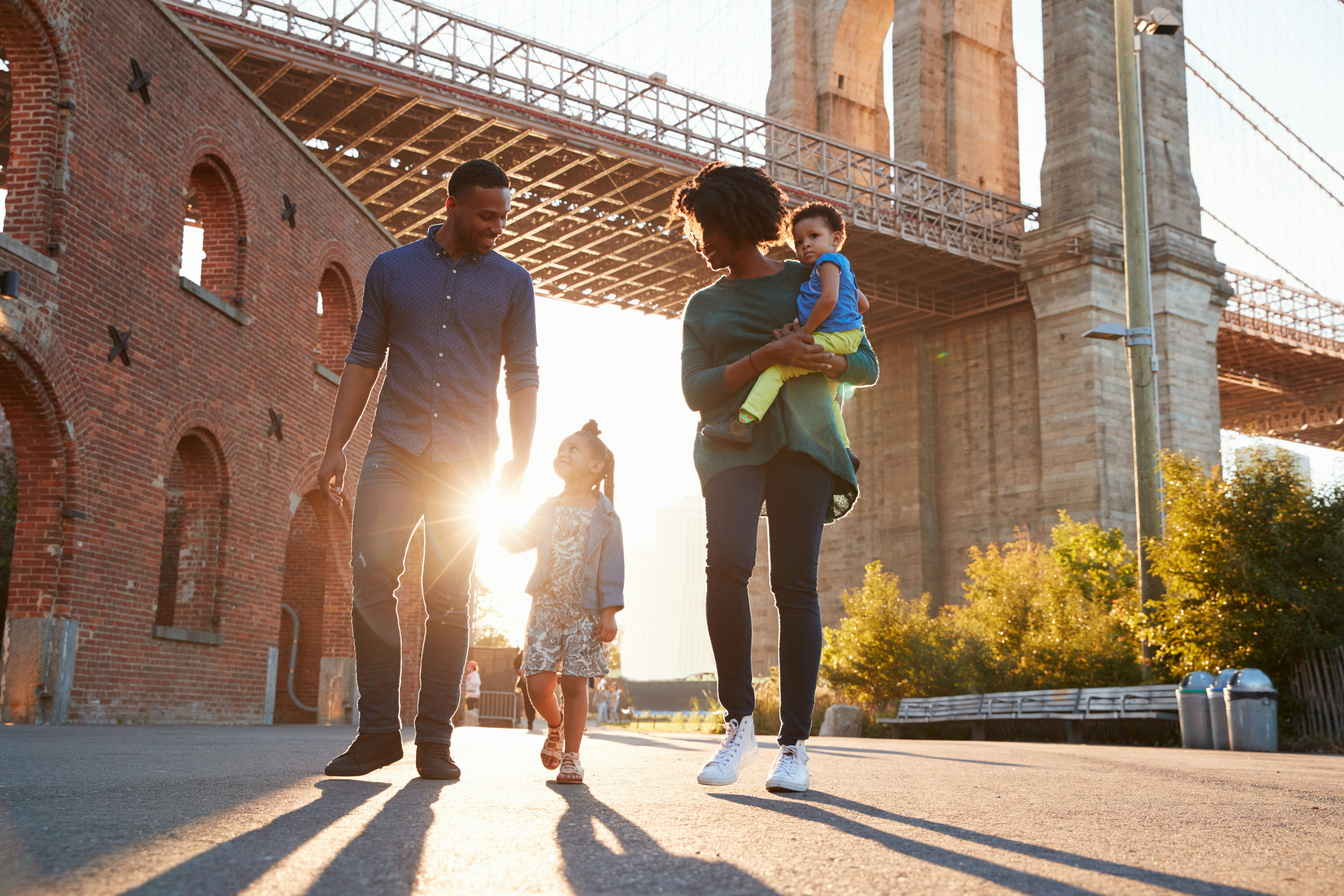 A family of four walks through the park under the Brooklyn Bridge  