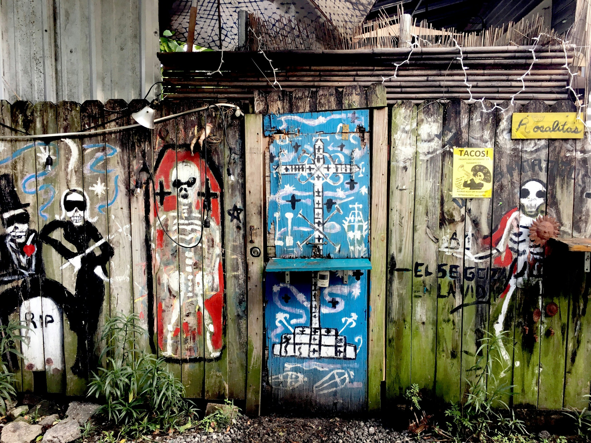 A weathered wooden fence is painted with bright skeletons in New Orleans