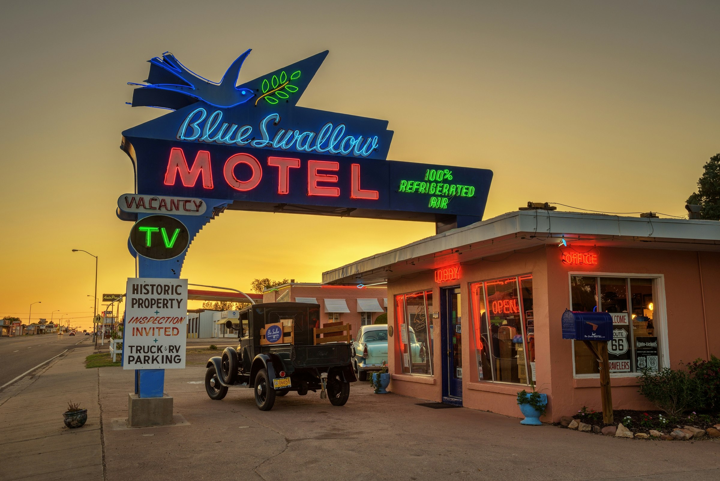 En exteriör bild av Blue Swallow Motel i New Mexico.  Motellet är litet men har en stor neonskylt som lockar bilisters uppmärksamhet, som kör längs motorvägen bredvid motellet.