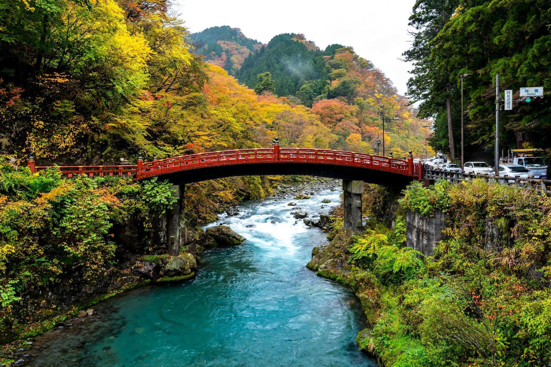 A red bridge spans a river and is surrounded by autumnal foliage in Nikko, Japan