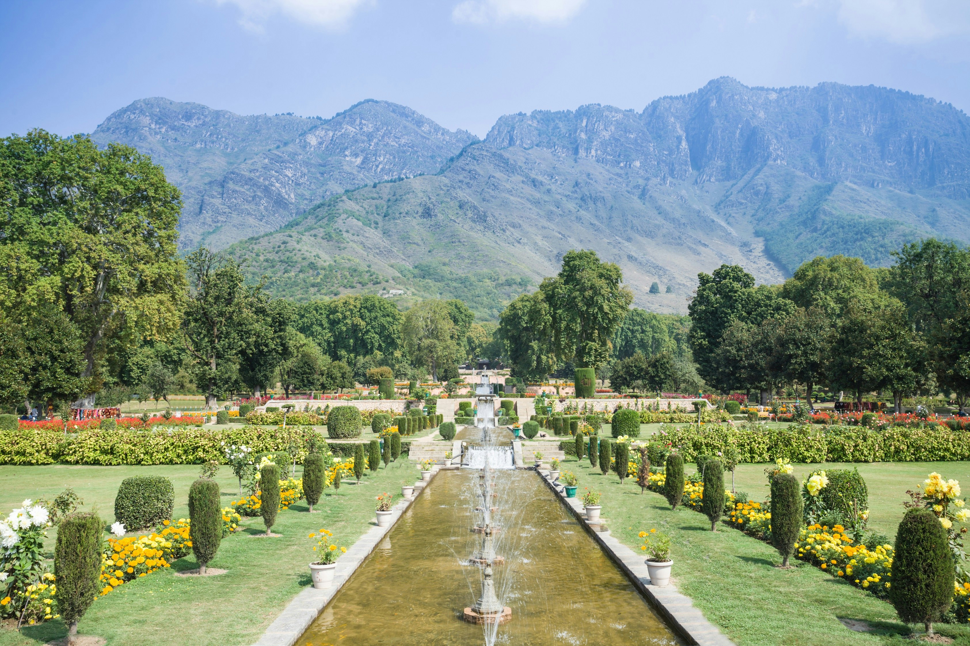 A view of the tiered central pond that runs down the centre of the long Nishat Bagh garden in Srinagar. The pond, which is filled with small fountains, is surrounded by flowers and bushes.