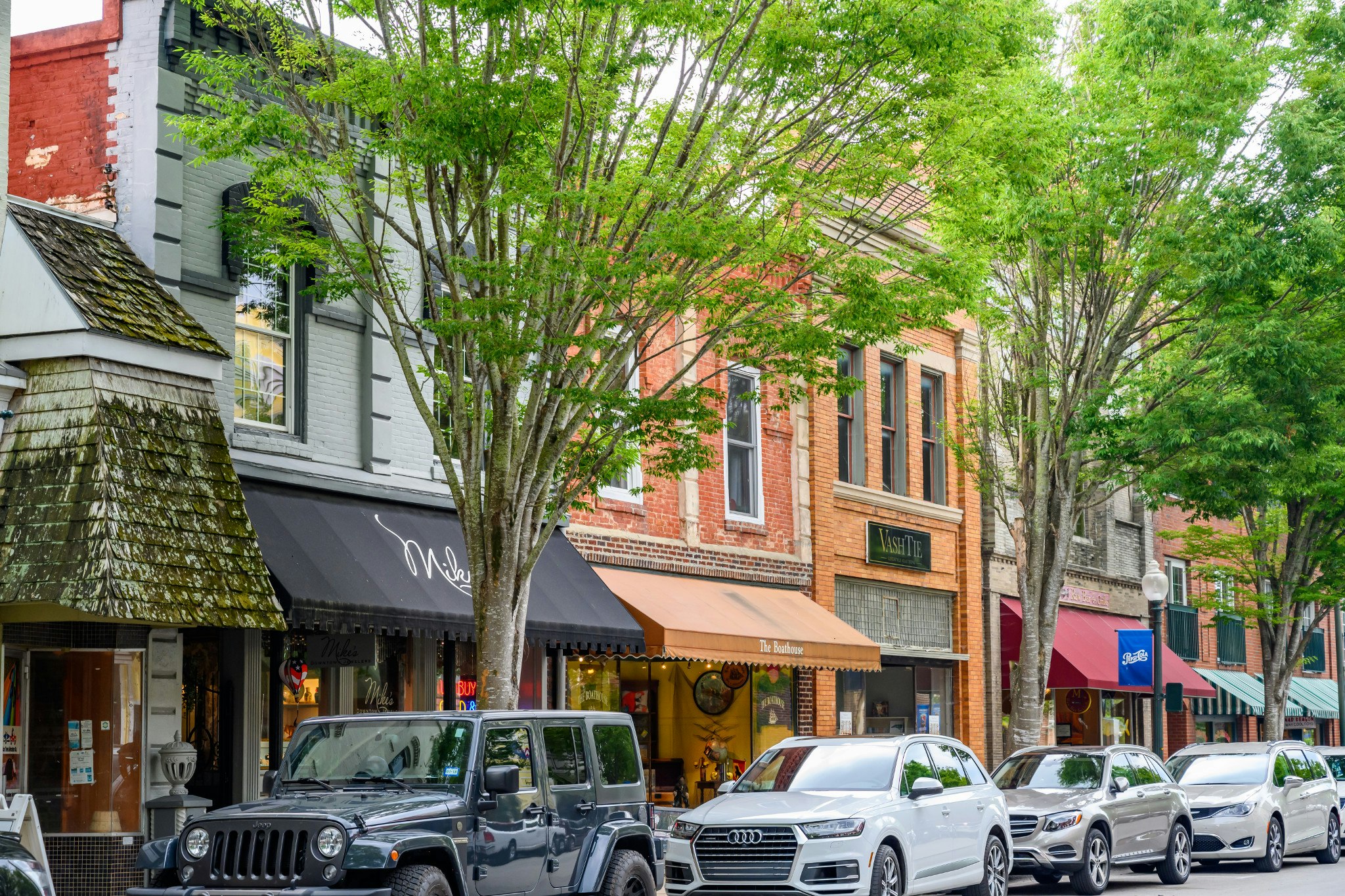 A retail street in North Carolina. A line of cars are parked on the sidewalk. 