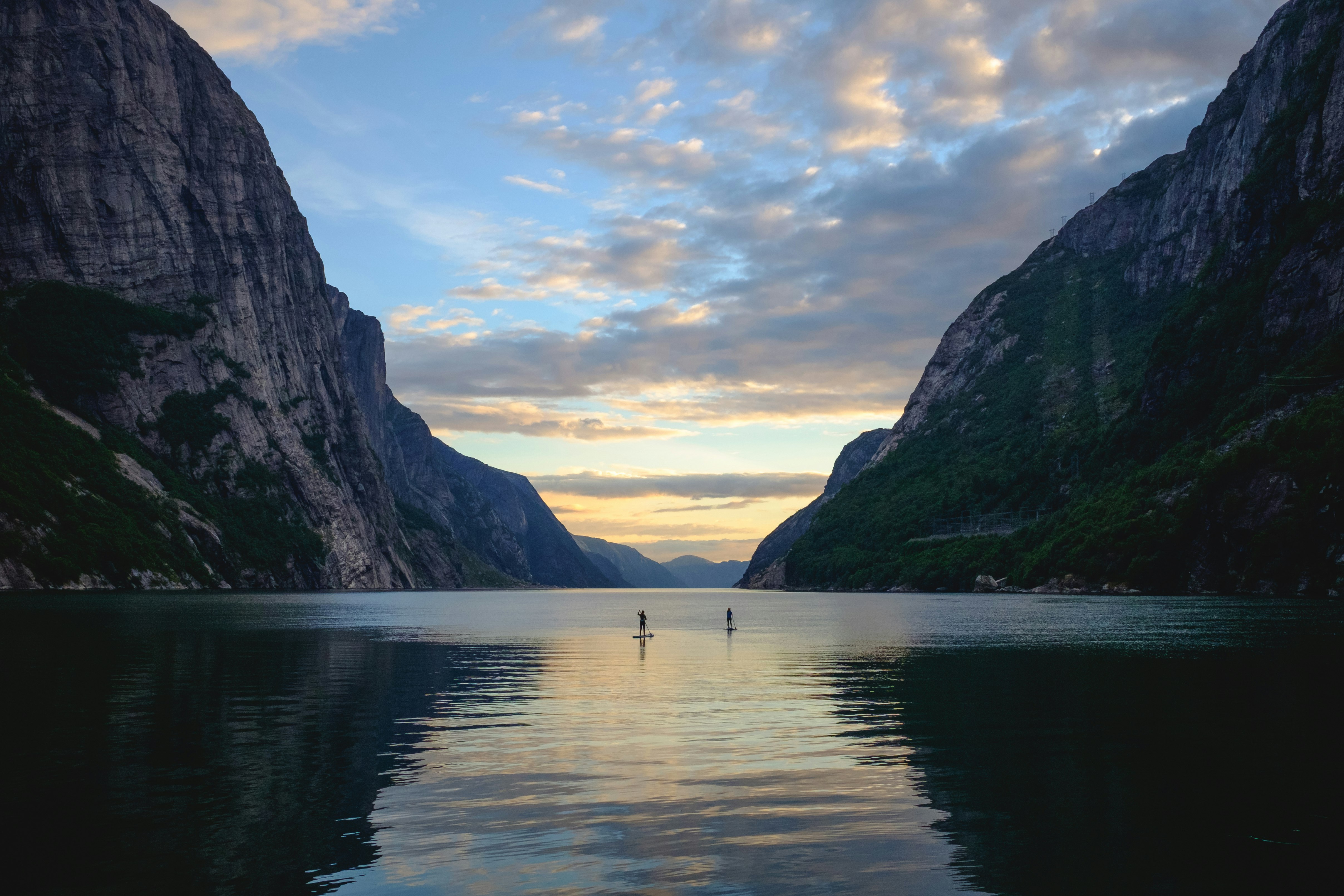 Scenic View Of Fjord By Mountains Against Sky with two paddle boarders punting up the middle; places to go stand up paddle boarding