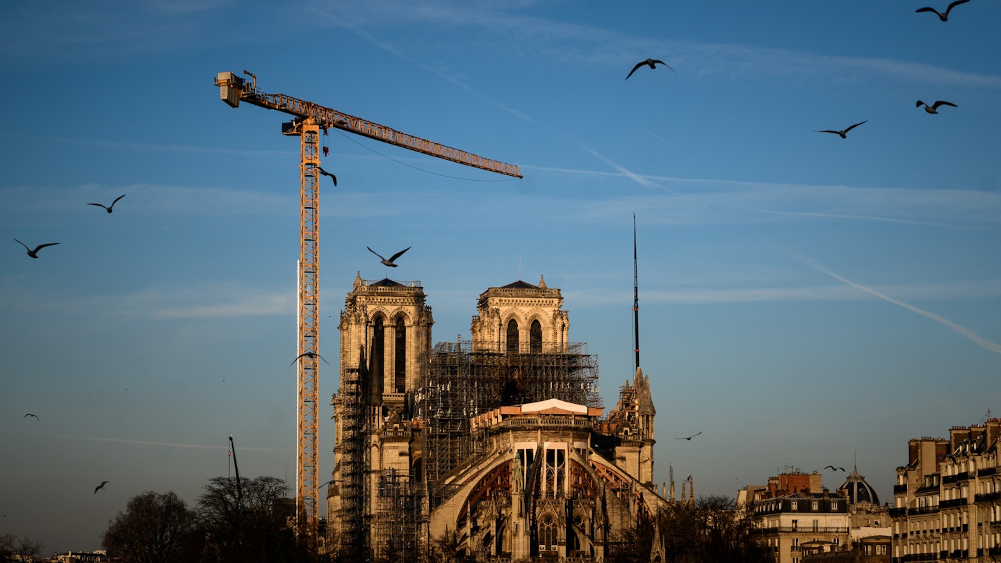 Notre-Dame Cathedral in Paris on January 6, 2020, covered in scaffolding with a crane in front and birds overhead