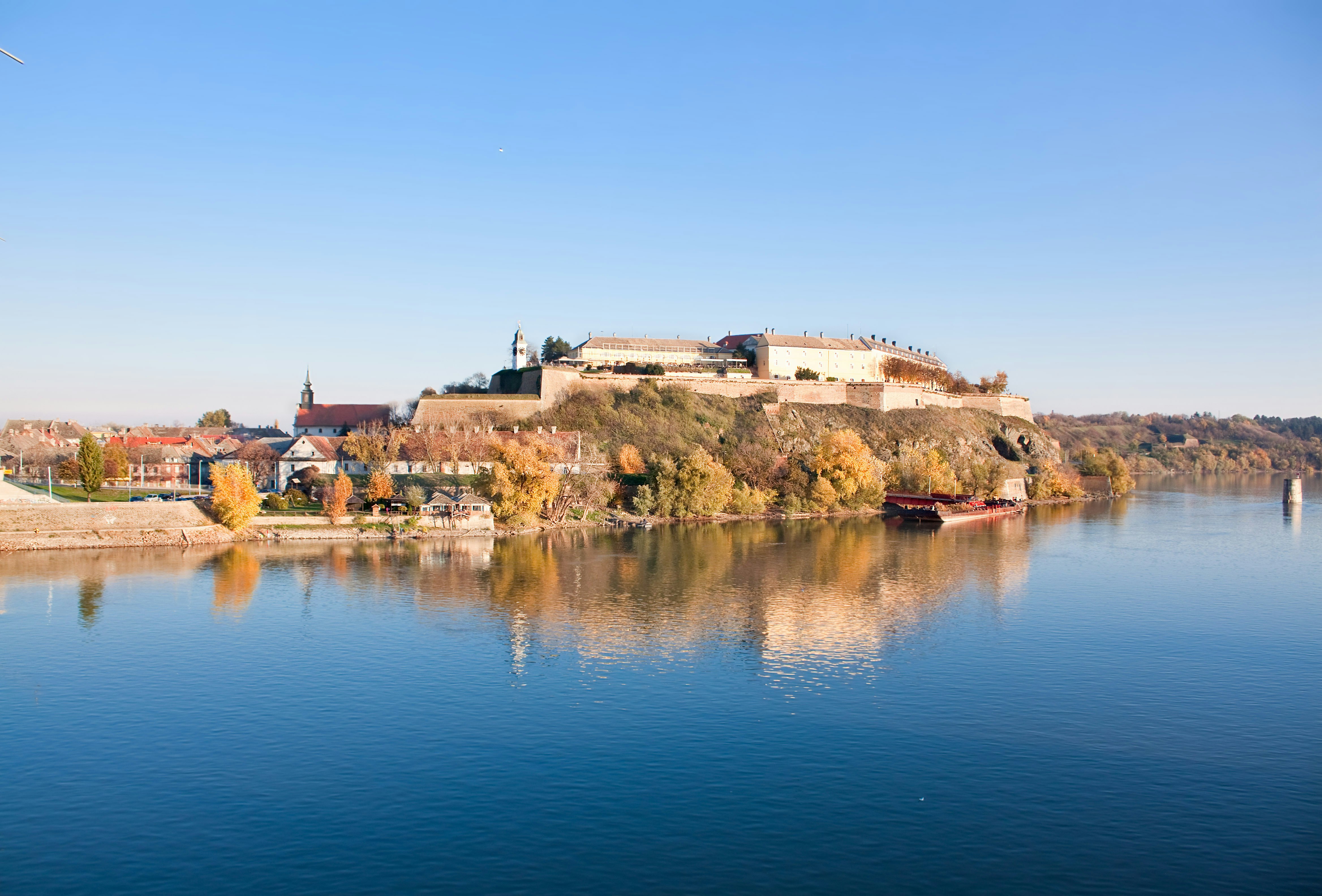 A wide blue river is in the foreground with a large brick fortress dominating the opposite bank