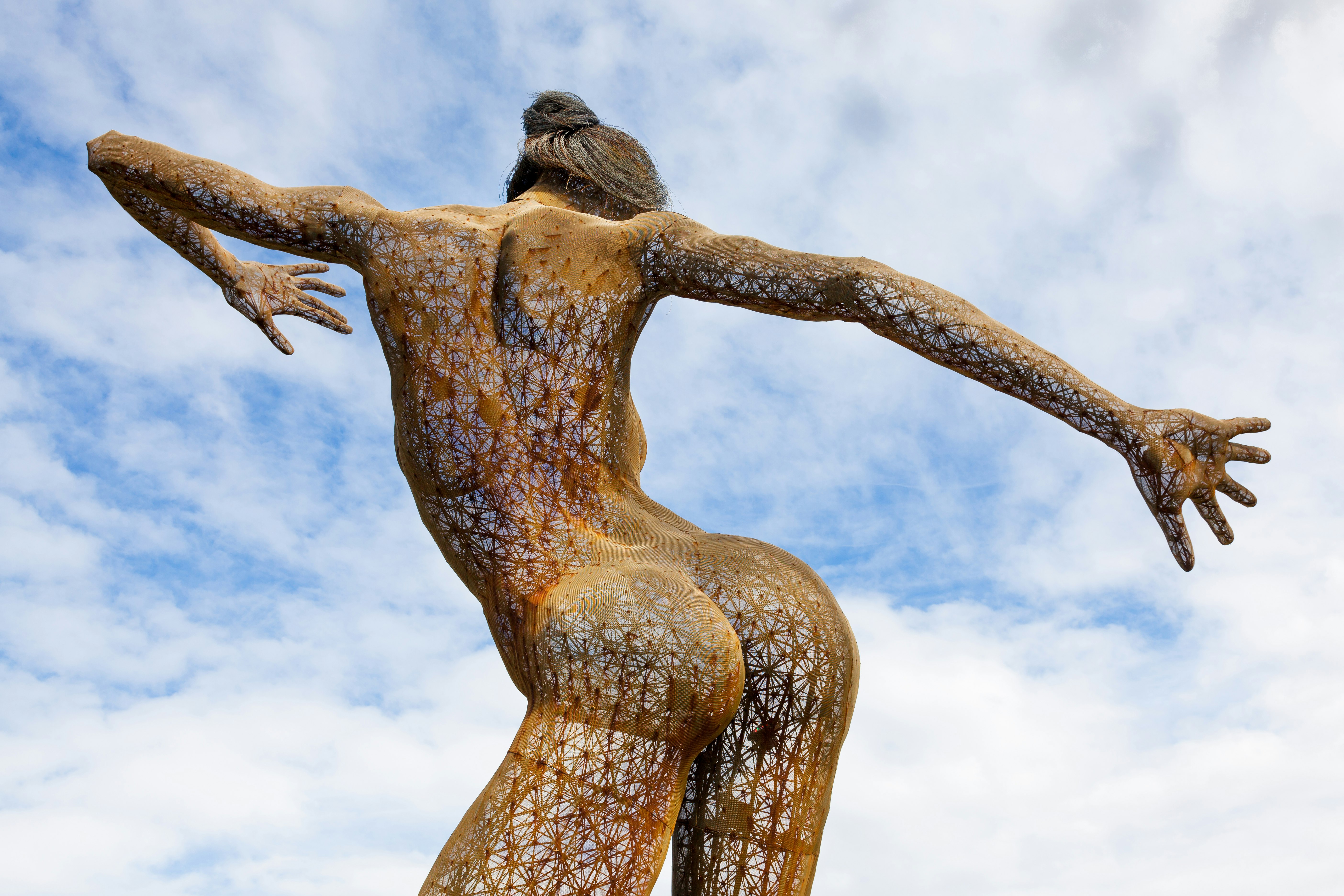A large mesh sculpture in the form of a woman stands 40-feet high with her arms spread wide apart 